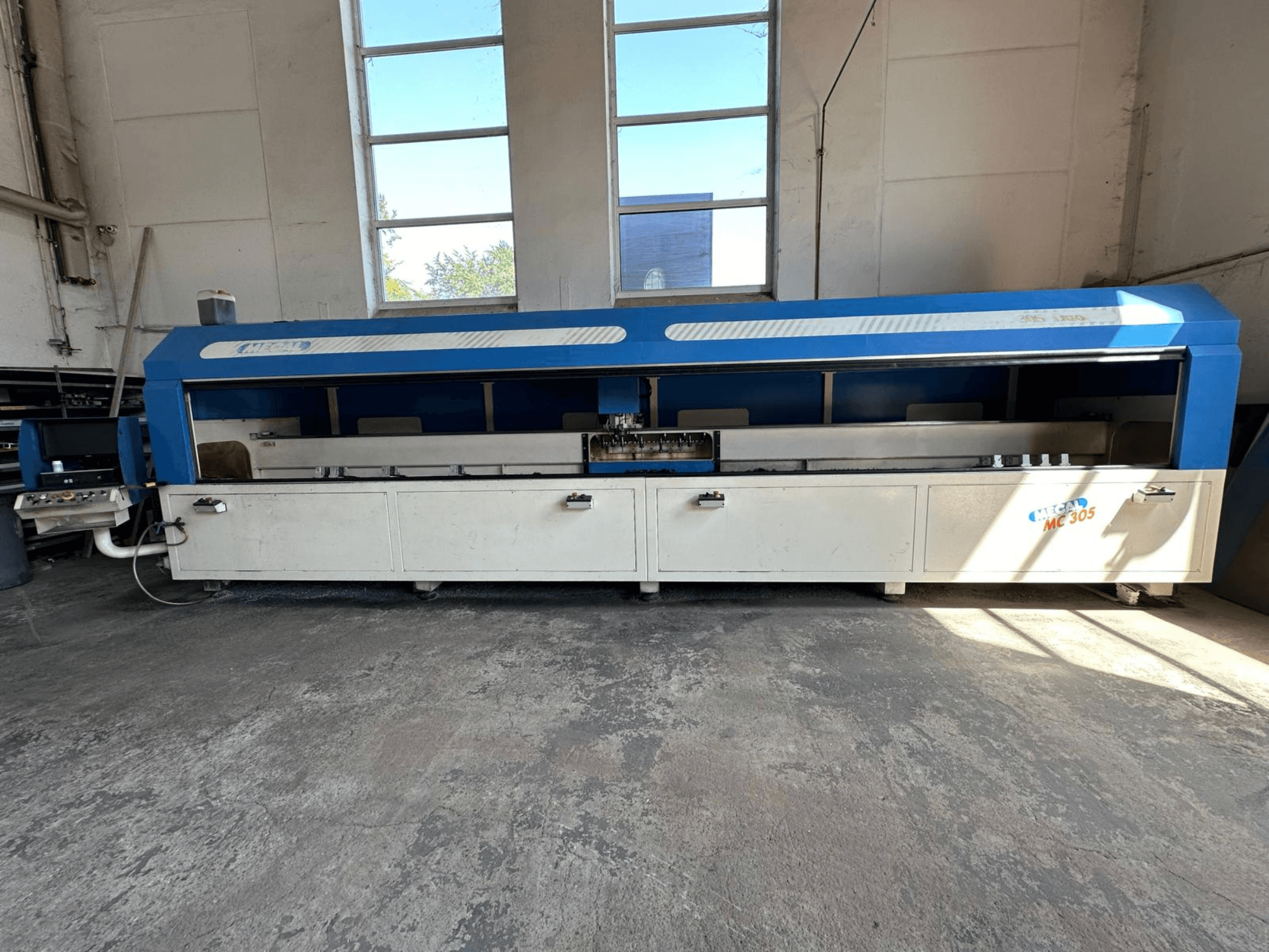 Frontansicht des vertikalen Bearbeitungszentrums MECAL MC 305 mit blau-weißem Design, sichtbarem Arbeitstisch und Bedienfeld.