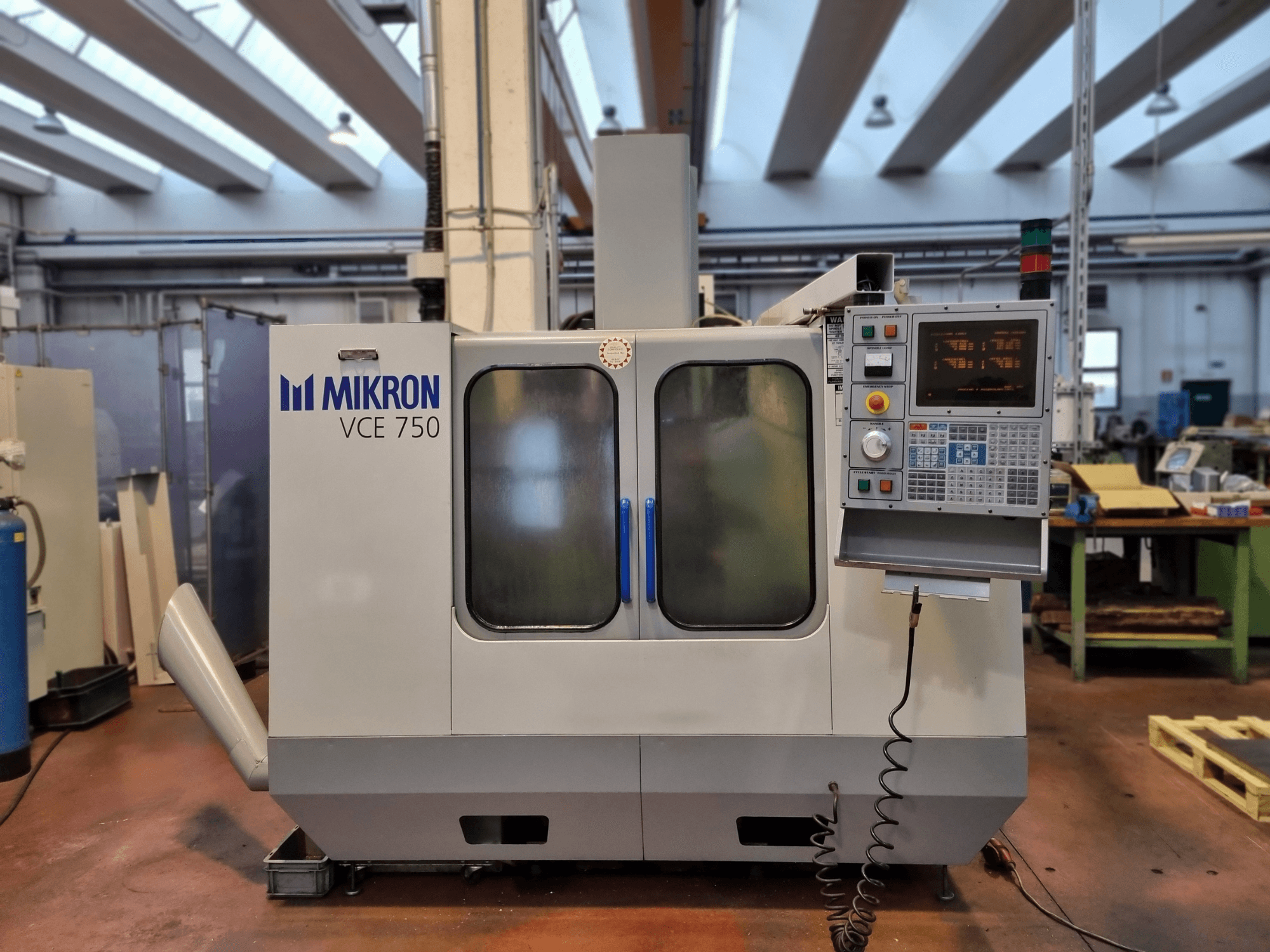 Weiße CNC-Maschine Mikron VCE 750 in einer Werkstatt, Seitenansicht, mit digitalem Bedienfeld und großen Glastüren.