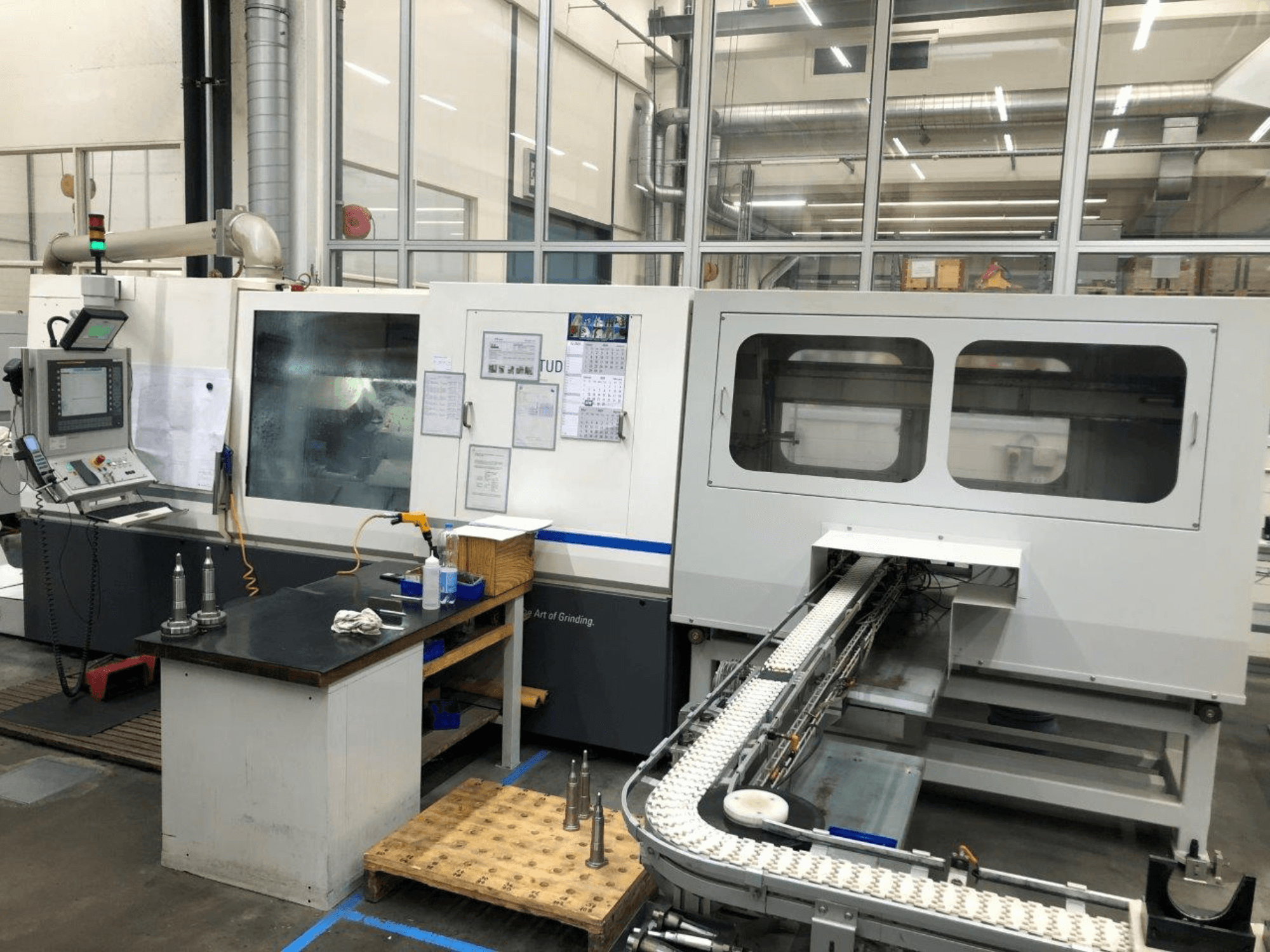 CNC grinding machine with control panel, front view; features a conveyor and clear viewing windows, showcasing precision tools.