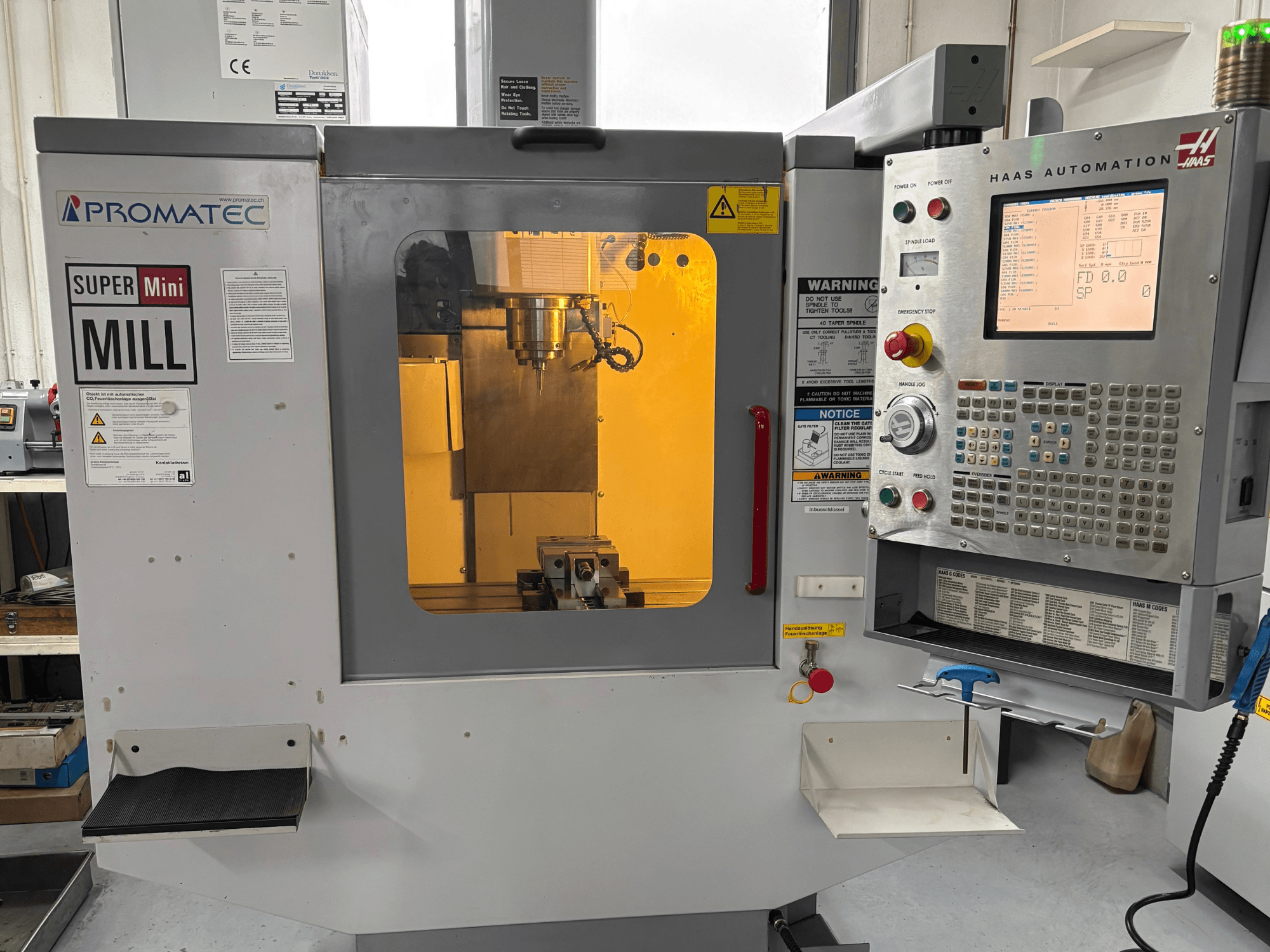 Promatec Super Mini Mill in der Vorderansicht, ausgestattet mit einem Haas Automation Bedienfeld und sichtbarem Schneidwerkzeug im Inneren.