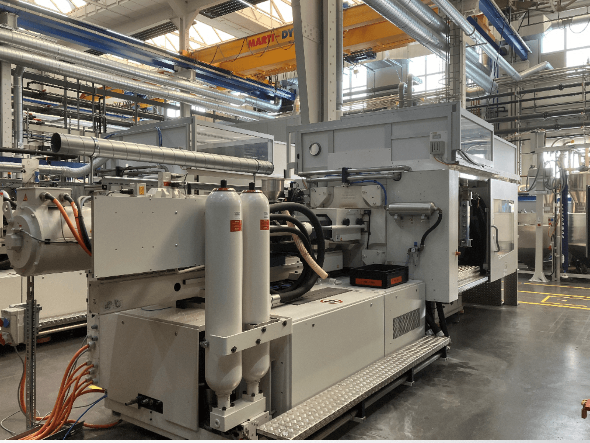 Industrial machine shown in side view with multiple hoses, two vertical tanks, and control panel; brand/model not visible.