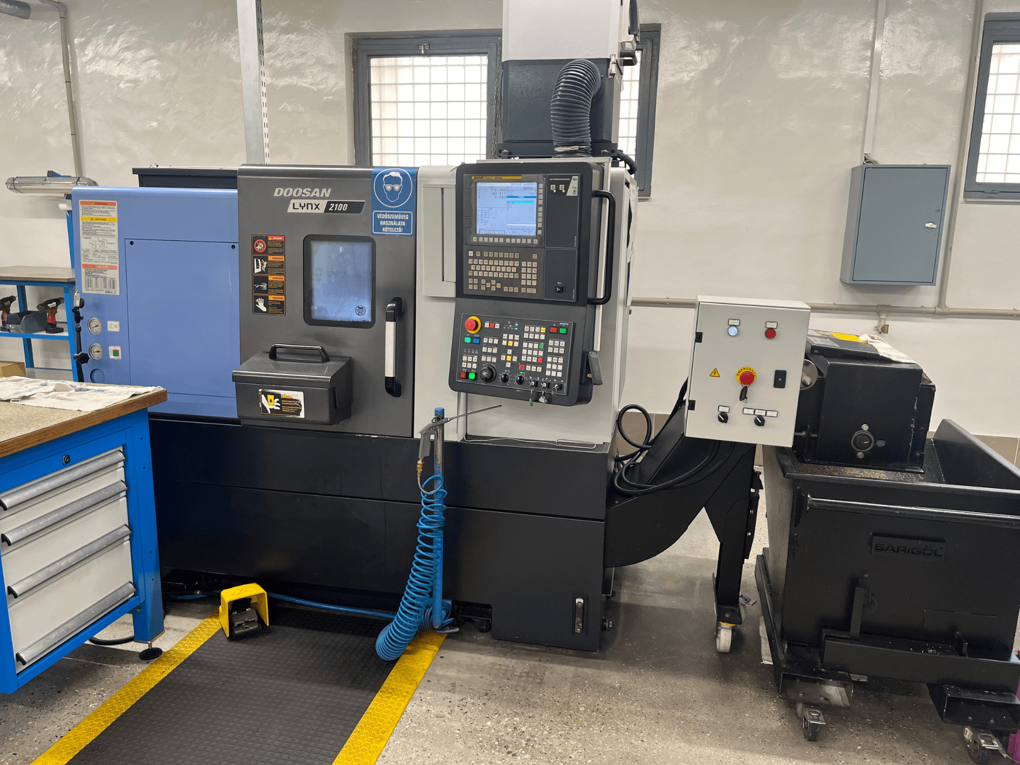 Doosan Lynx 210 lathe in workshop, showing control panel, tool storage, and coolant system, side view with workspace details.