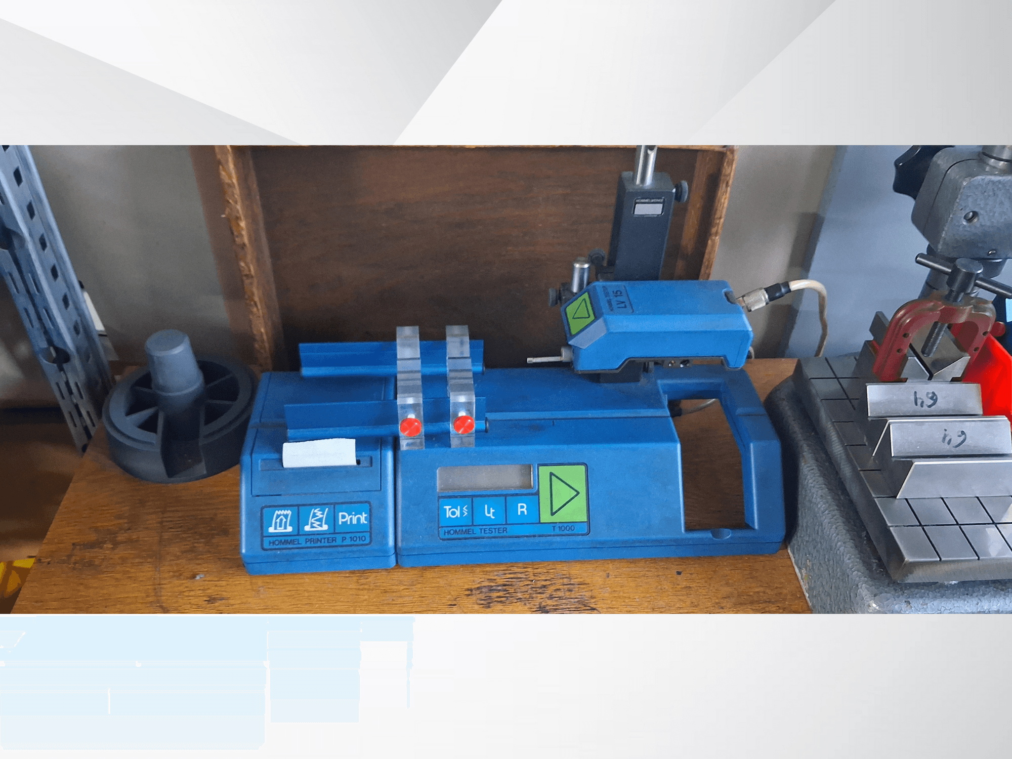 Blauer Hommel T 1000 Drucker und T 1 010 Tester mit roten Tasten, von vorne gesehen auf einer Werkbank mit Metallblöcken.