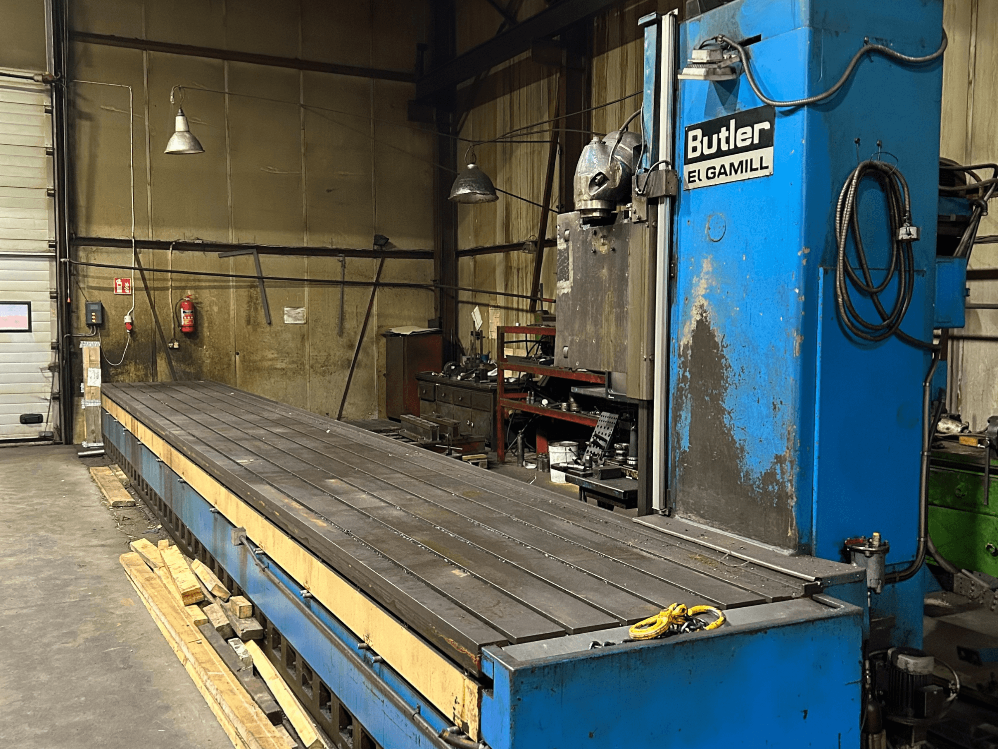 Blue Butler El Gamill milling machine in a workshop, side view showing a long flat table and controls on the right.