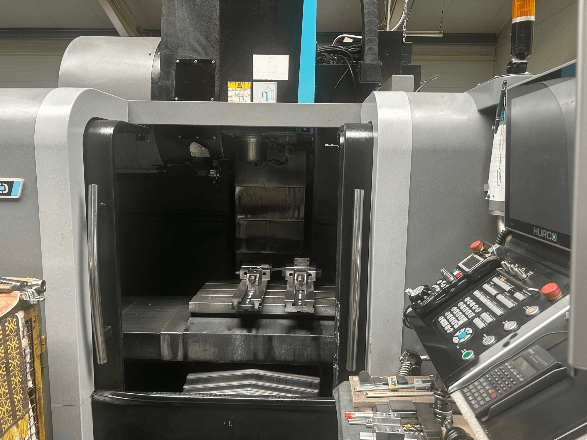 Frontansicht des Hurco CNC-Bearbeitungszentrums mit Werkzeughalter, Metallwerkstück und Bedienfeld mit Tasten und Display.