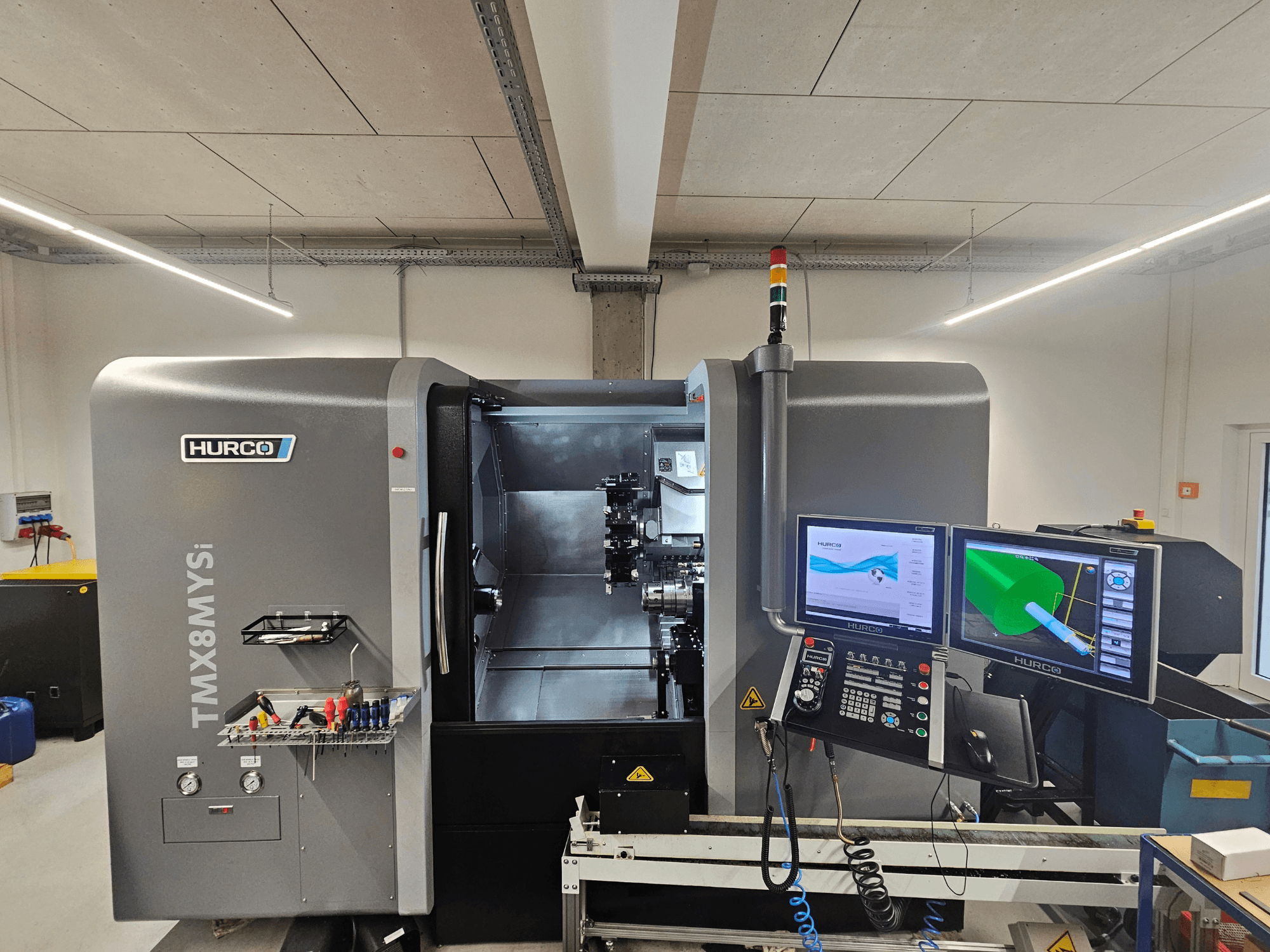 Hurco TMX 8 MYSi Dreh-Fräszentrum in einer Werkstatt, mit zwei Monitoren, Bedienfeld und Werkzeugen an der Seite.