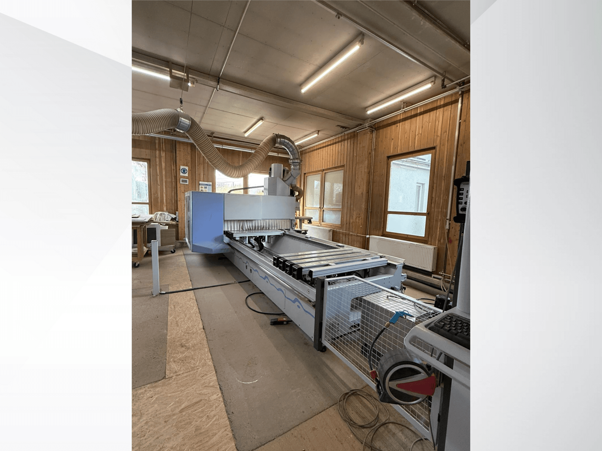 CNC milling machine in a workshop, side view, featuring a large blue body, attached belt conveyor, and visible control panel.