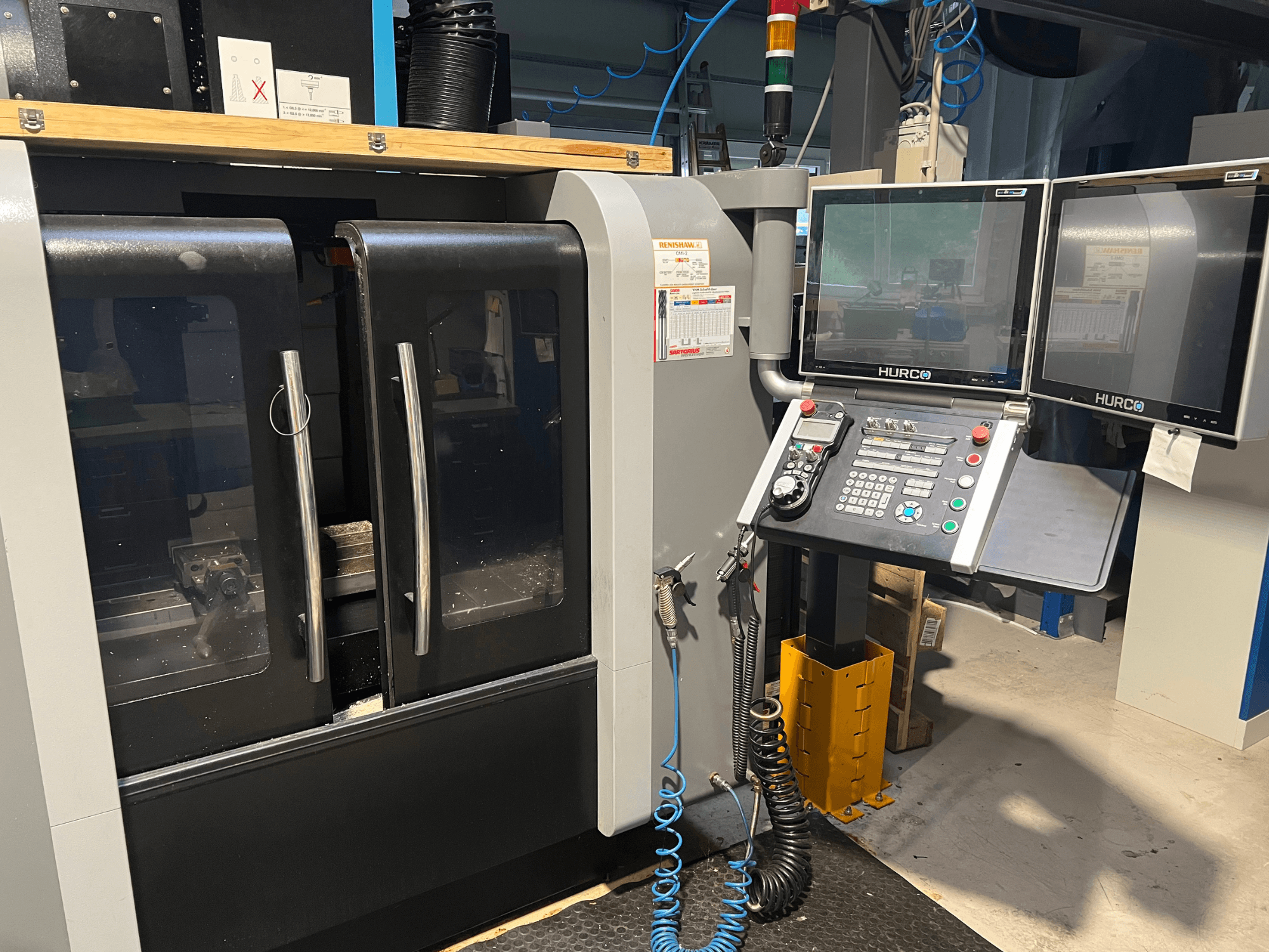 Frontansicht der Hurco CNC-Maschine mit zwei Monitoren und Bedienfeld. Mit durchsichtigen Türen und sichtbarem Bearbeitungsbereich im Inneren.