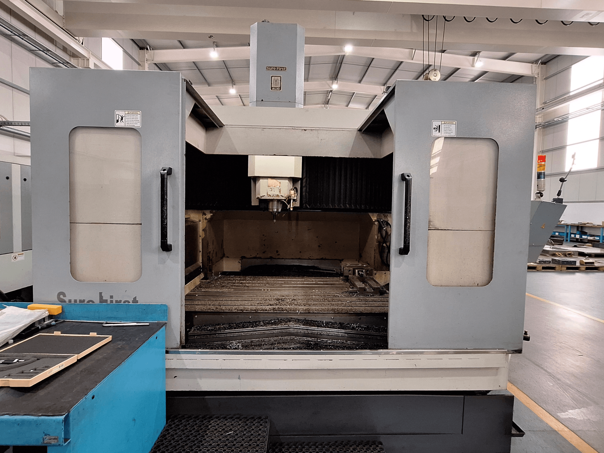 Vertikales Bearbeitungszentrum Sure First QM-1836, Vorderansicht mit Werkzeugkopf und leerem Arbeitsraum, moderne Industrieumgebung.