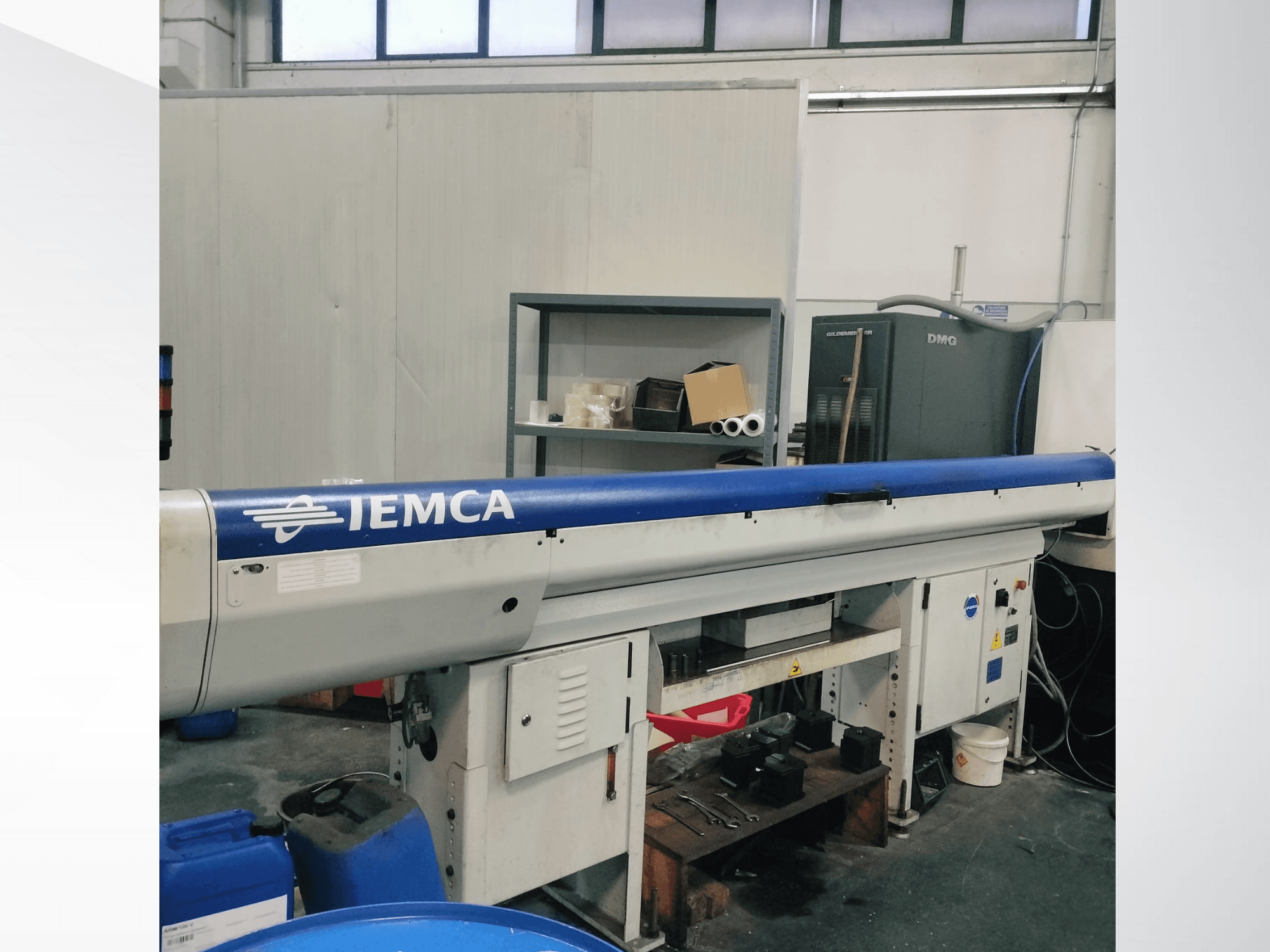 IEMCA automatic bar feeder seen from the front in a workshop, featuring a blue loading tube and a control panel.
