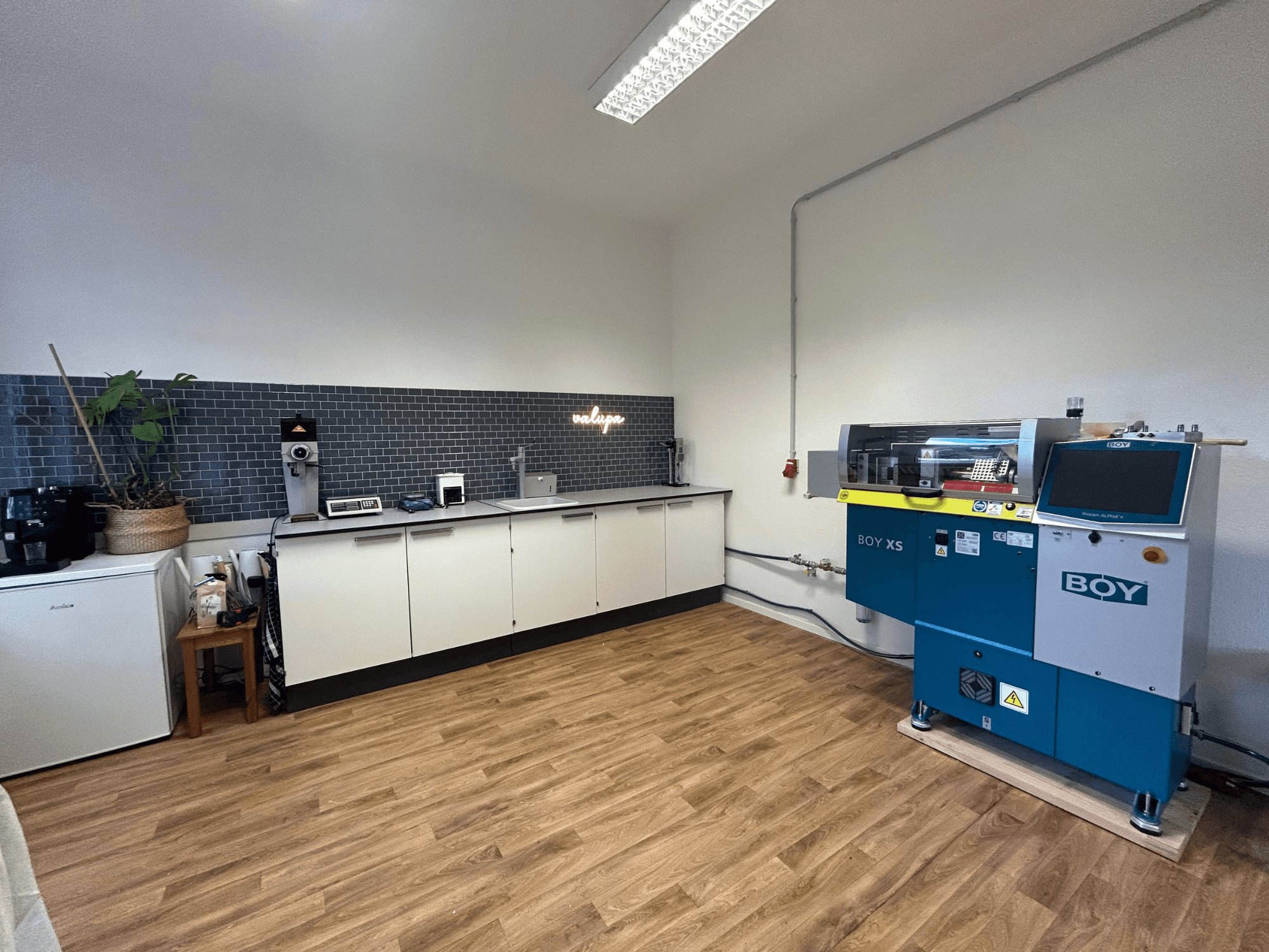 Hydraulischer Spritzgießautomat BOY XS 161, Vorderansicht, in einer modernen Kücheneinrichtung mit Geräten und Holzfußboden.