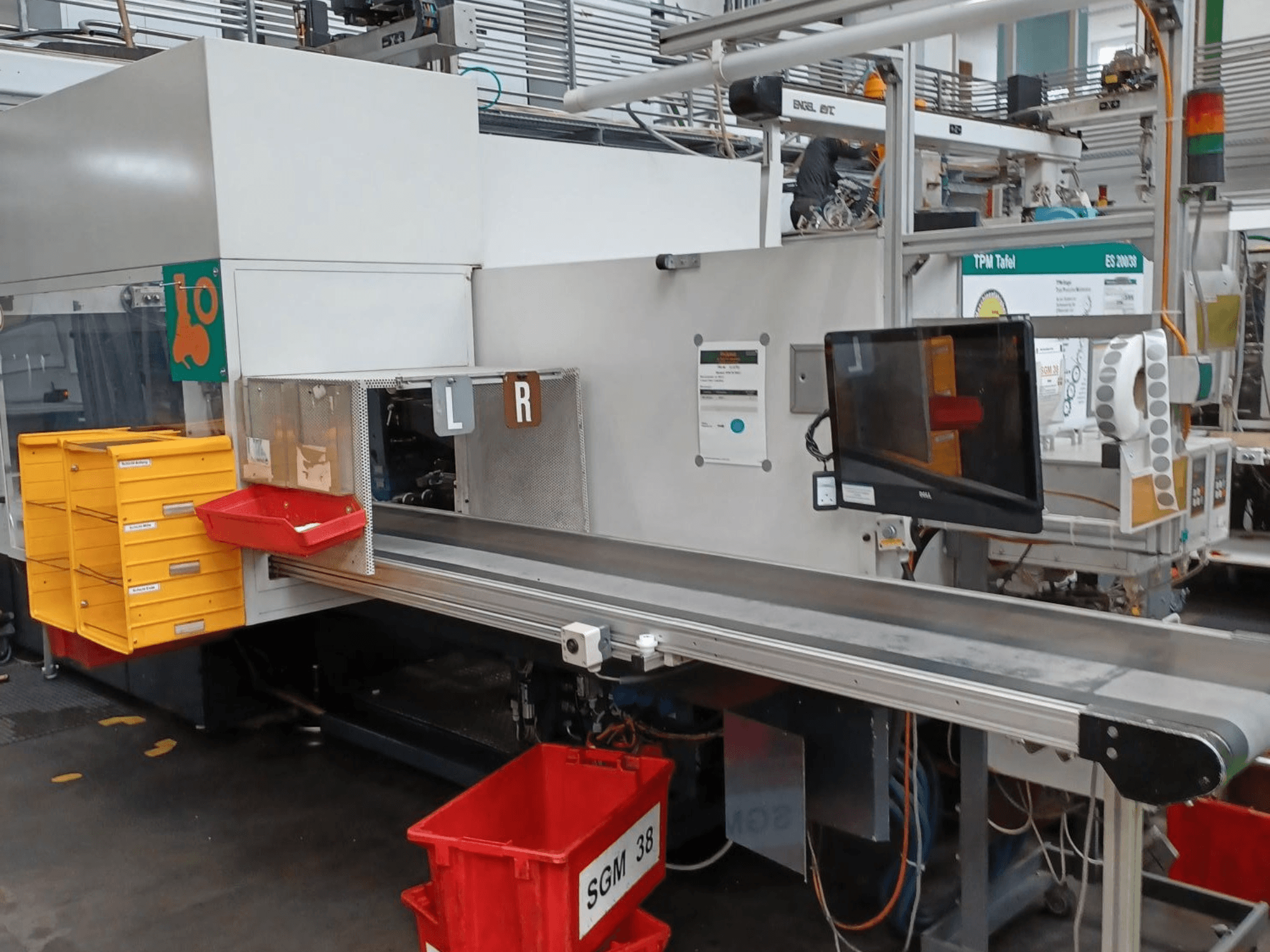 Industrielle Sortiermaschine mit gelben und roten Behältern, Seitenansicht, mit Kontrollmonitor und beschrifteten Fächern zum Sortieren.