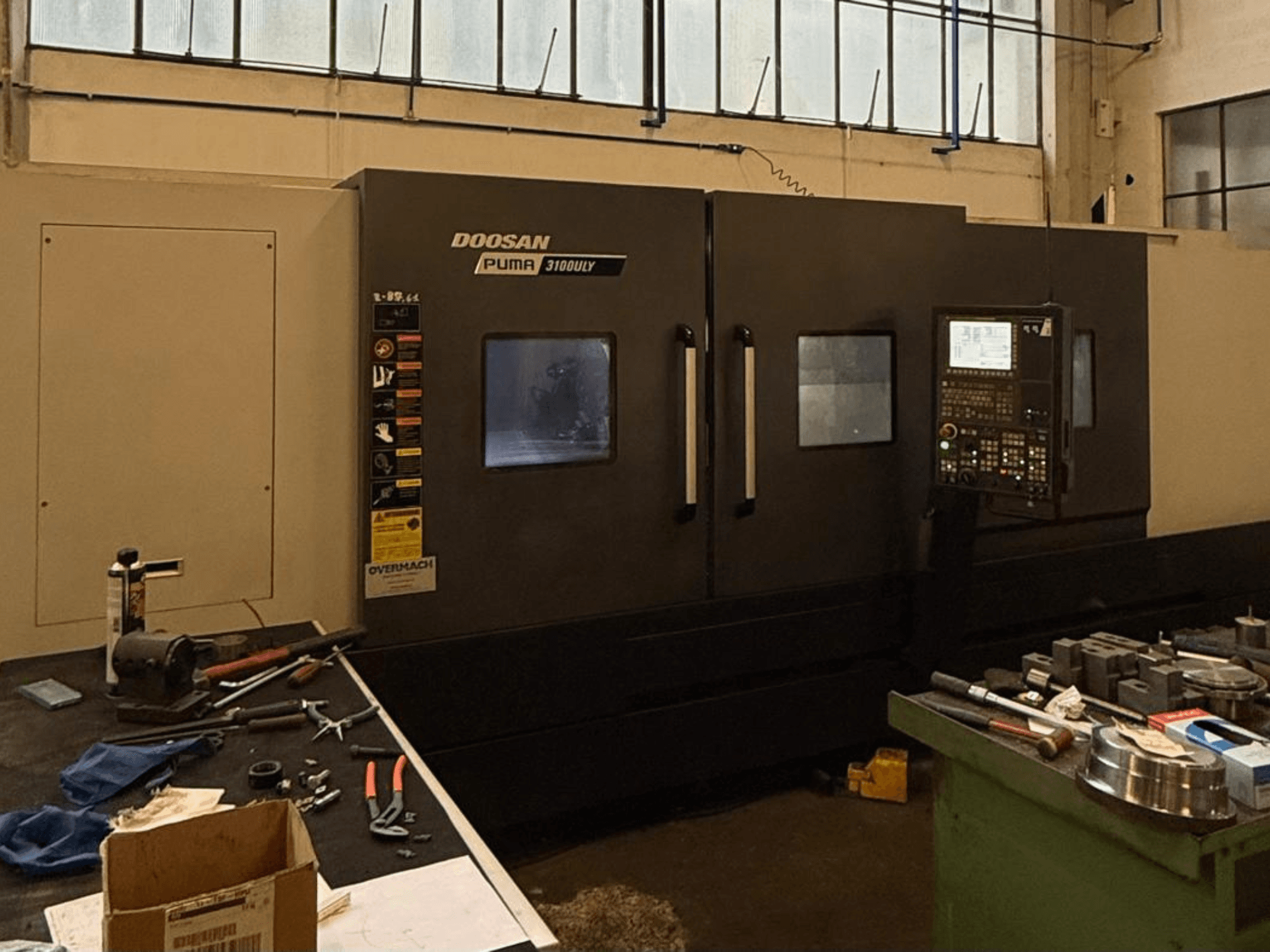 Doosan Puma 3100LY CNC-Drehmaschine in einer Werkstatt, Seitenansicht, mit Bedienfeld und Werkzeugen auf der Werkbank.