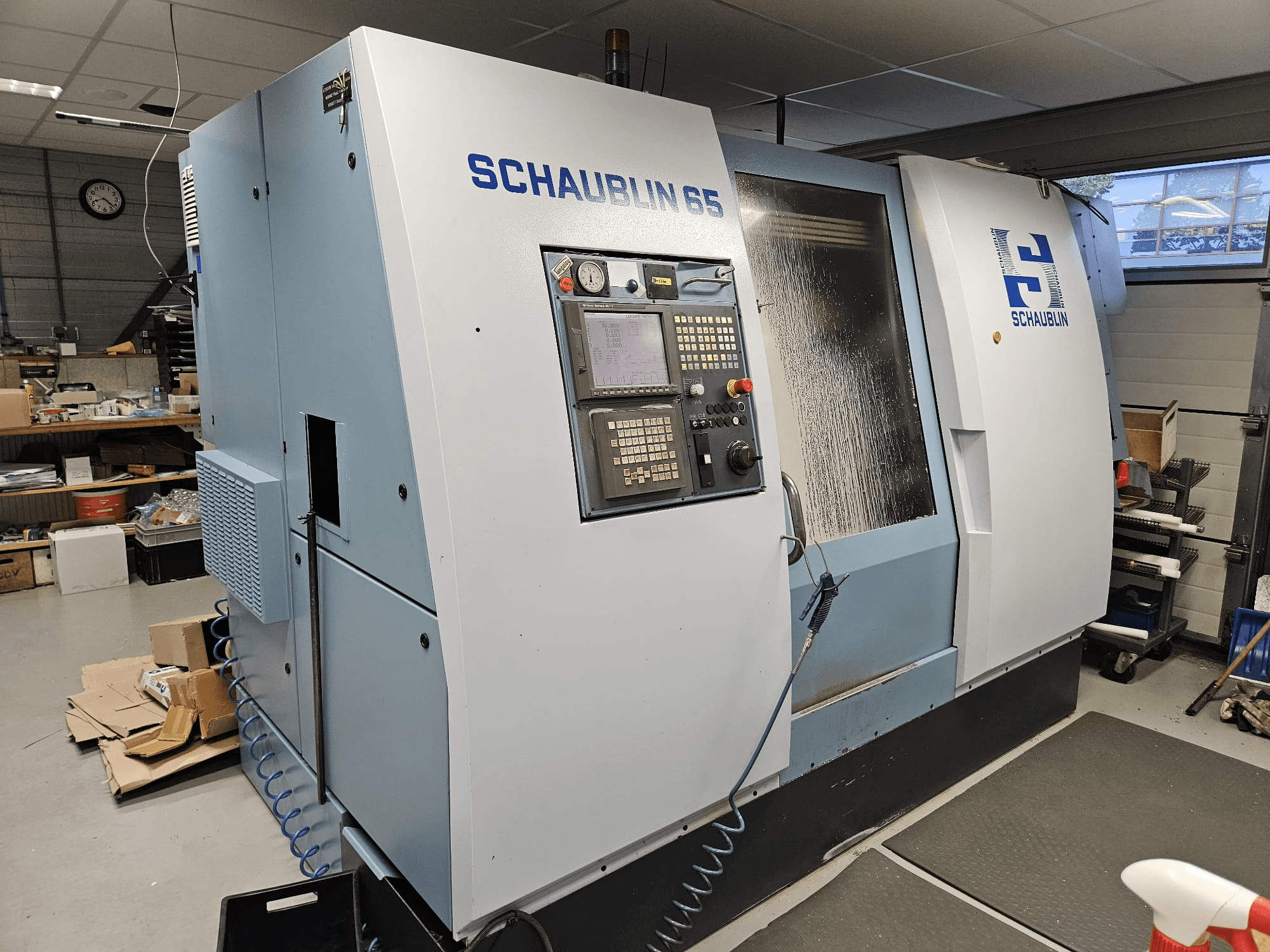 SCHAUBLIN 65 CNC machine, side view, featuring control panel, blue and grey casing, and visible coolant system.