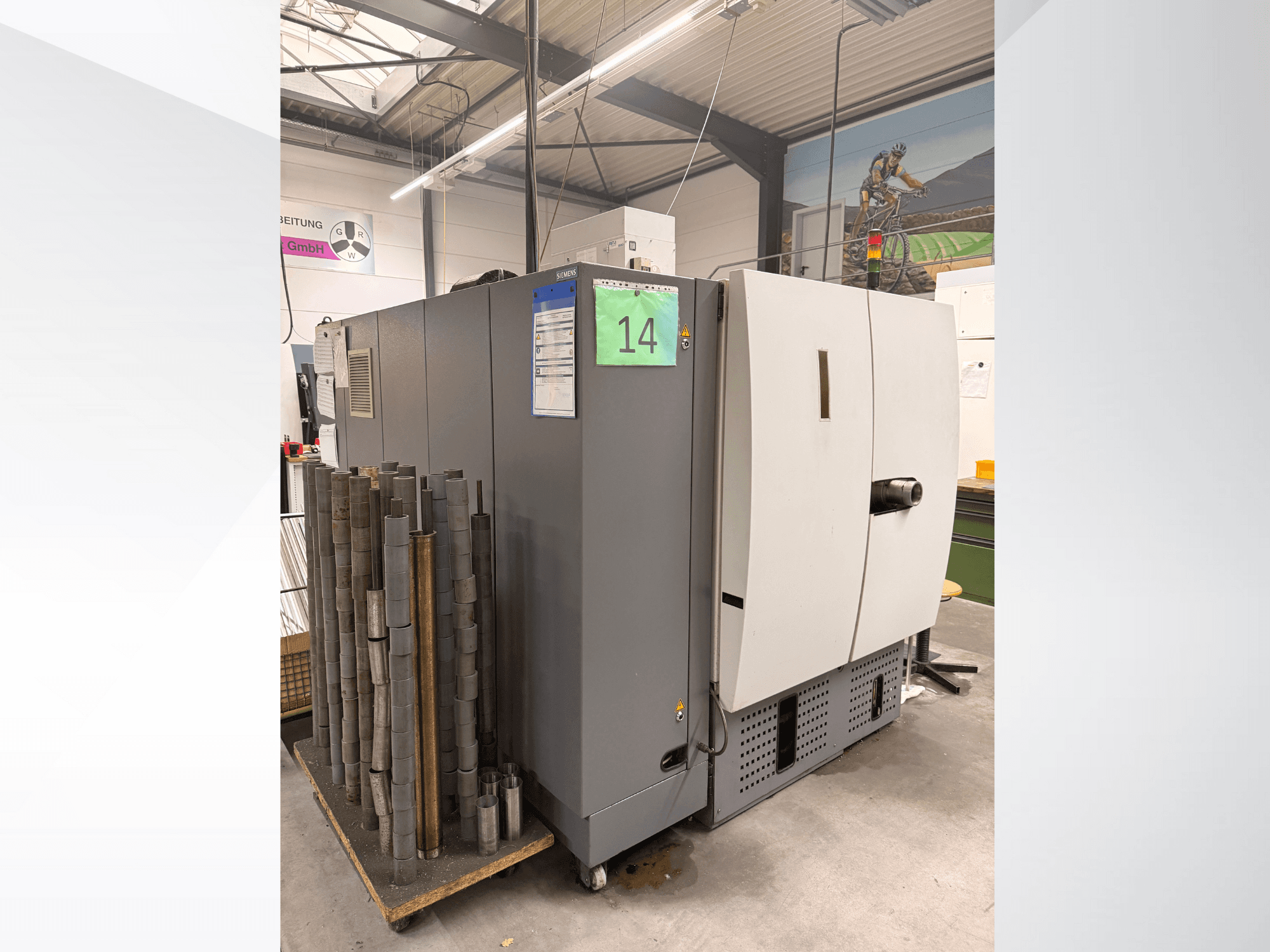 Gray industrial machine from Siemens, side view, with stock of cylindrical metal pieces beside it and equipment labels visible.