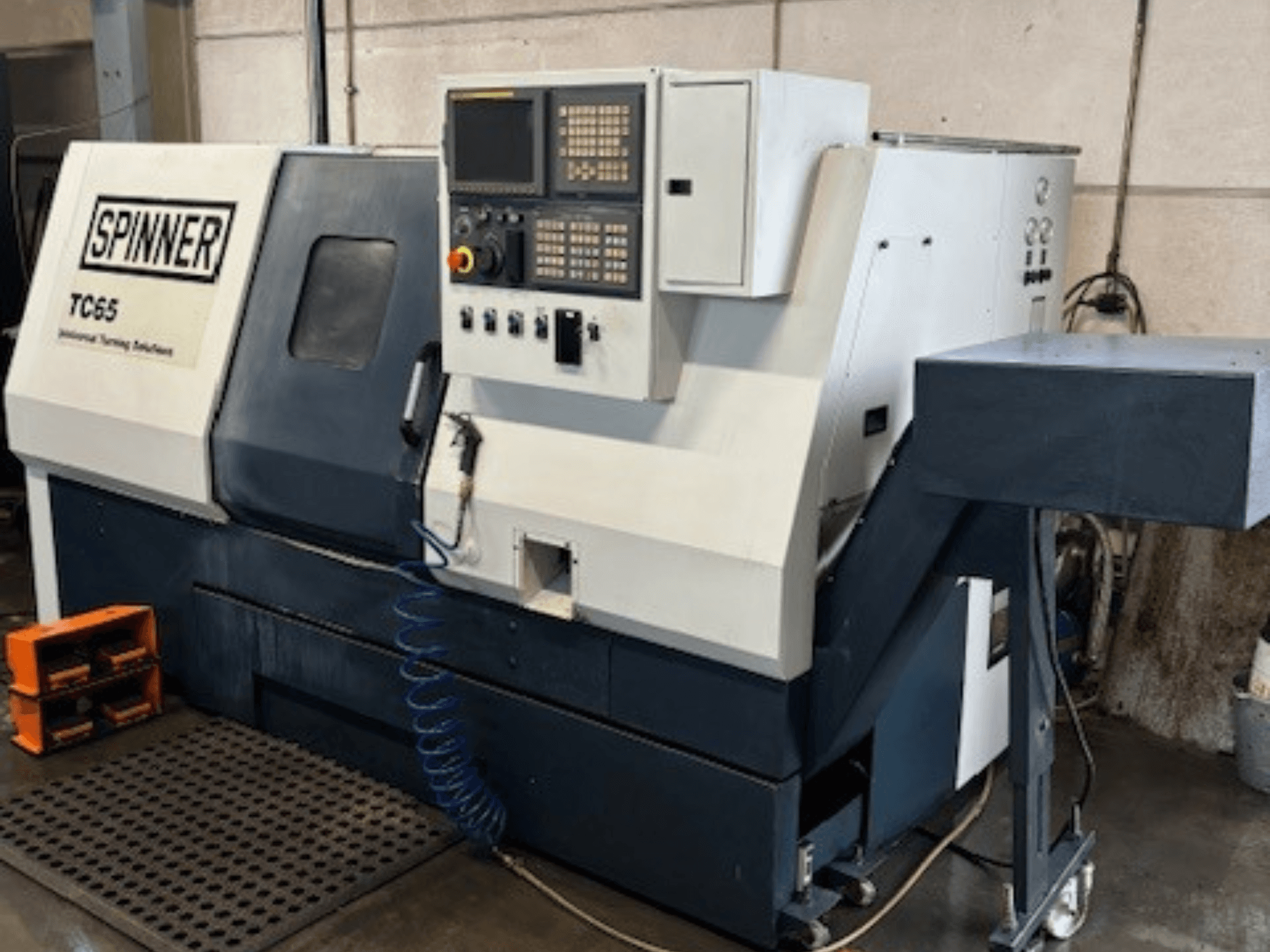 Spinner TC65 industrial turning machine, front view, features control panel, compressed air line, and tool storage area.
