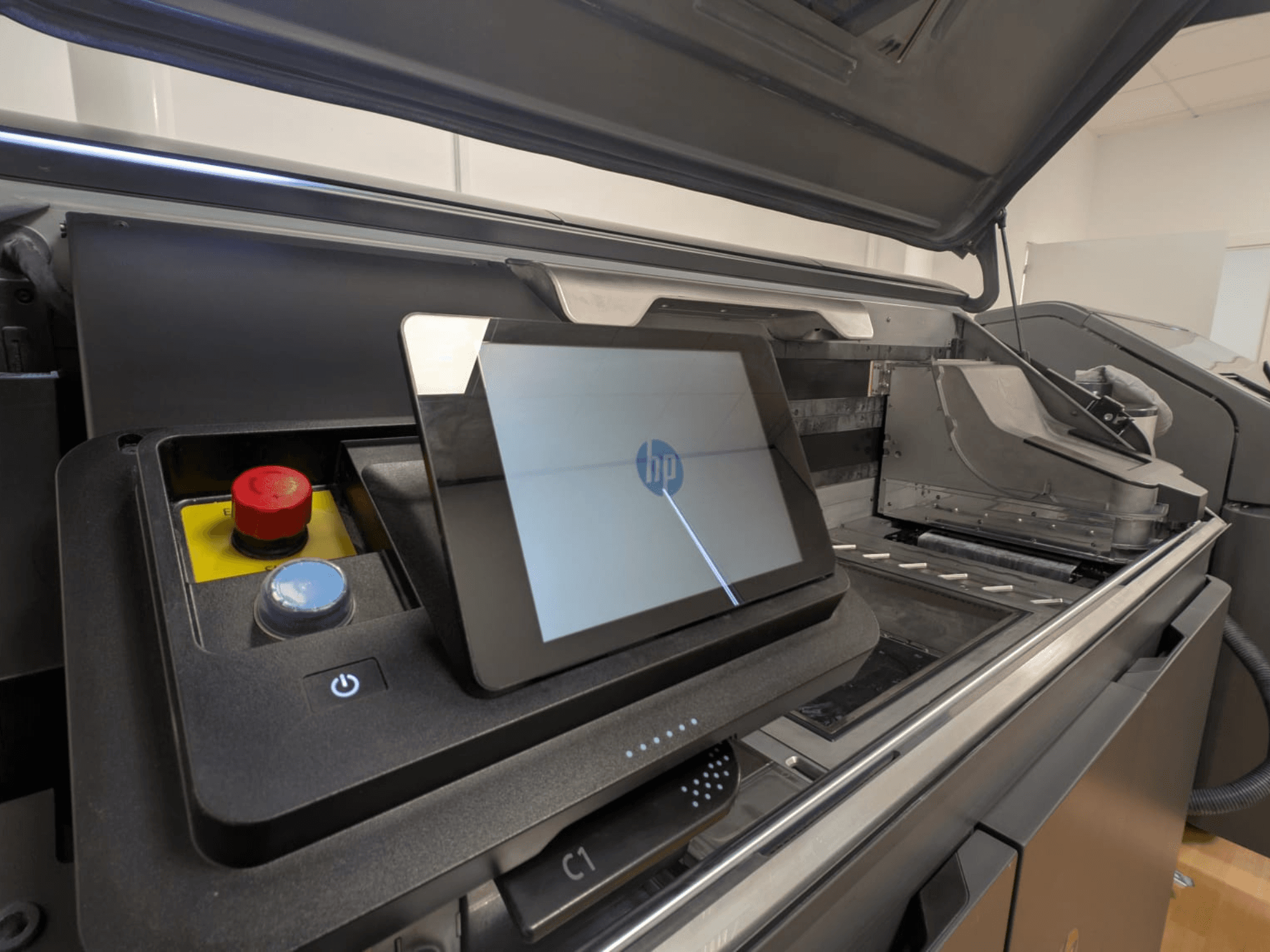 Das Bedienfeld des HP Druckers zeigt ein Tablet-Display, rote und blaue Tasten sowie eine Seitenansicht der inneren Komponenten des Druckers.