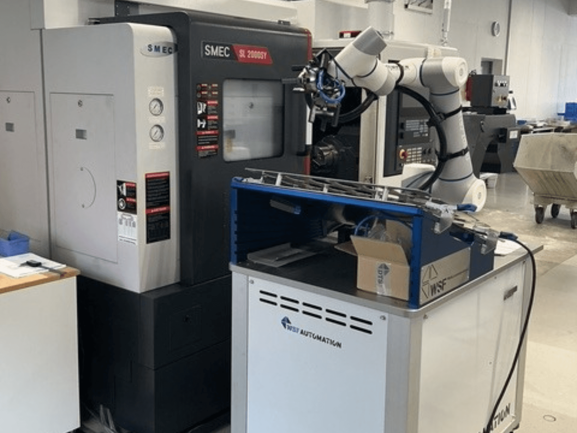 SMEC SL 2000SY machining center with a robotic arm on a blue workstation, viewed from the front in a workshop setting.