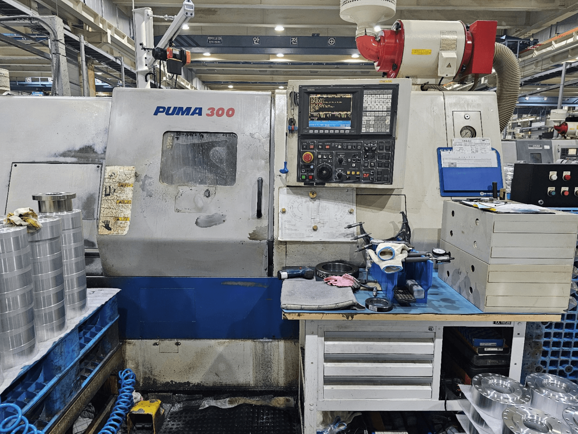PUMA 300 CNC-Maschine in einer Werkstatt; Vorderansicht mit Bedienfeld, Werkzeugen und Metallteilen auf einer Werkbank.