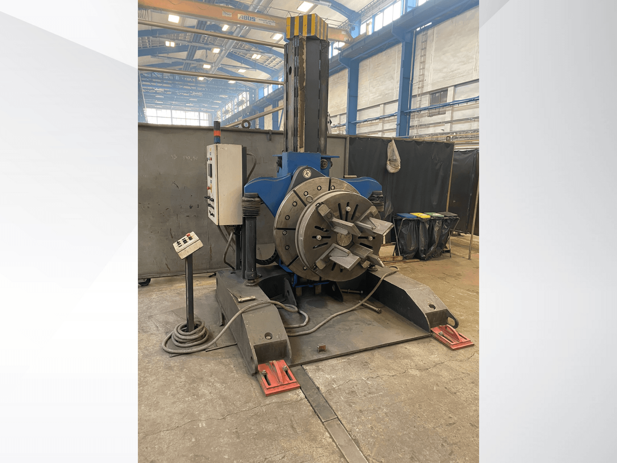 Blaue Industriedrehmaschine mit rundem Drehkopf und Bedienfeld, Seitenansicht, in einer Werkstattumgebung.