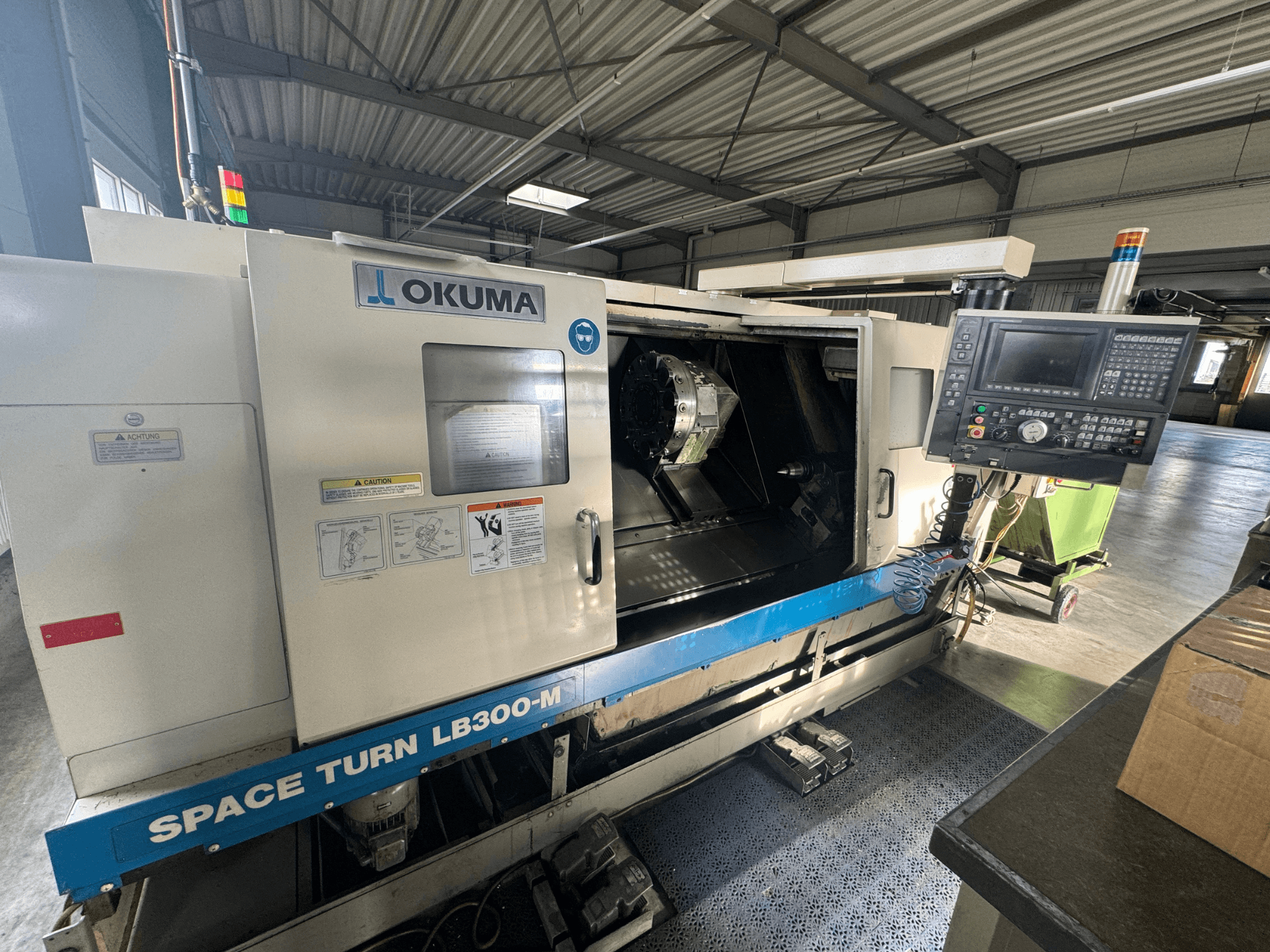Okuma Space Turn LB300-M CNC lathe in front view, featuring control panel and open door revealing interior machining area.