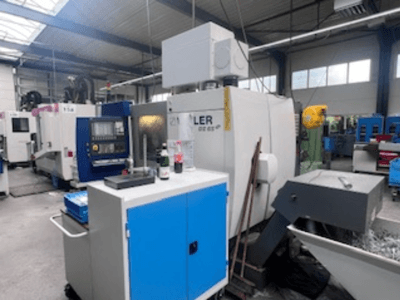 Industrial workshop with a Heller machining center, front view showing tools, controls, and surrounding equipment.