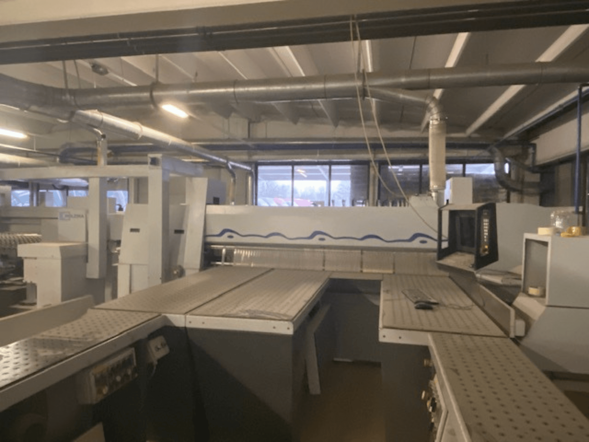 Industrieller Arbeitsplatz mit einer Maschinenanlage und einem Bedienpult, aus einem erhöhten Blickwinkel von vorne betrachtet.