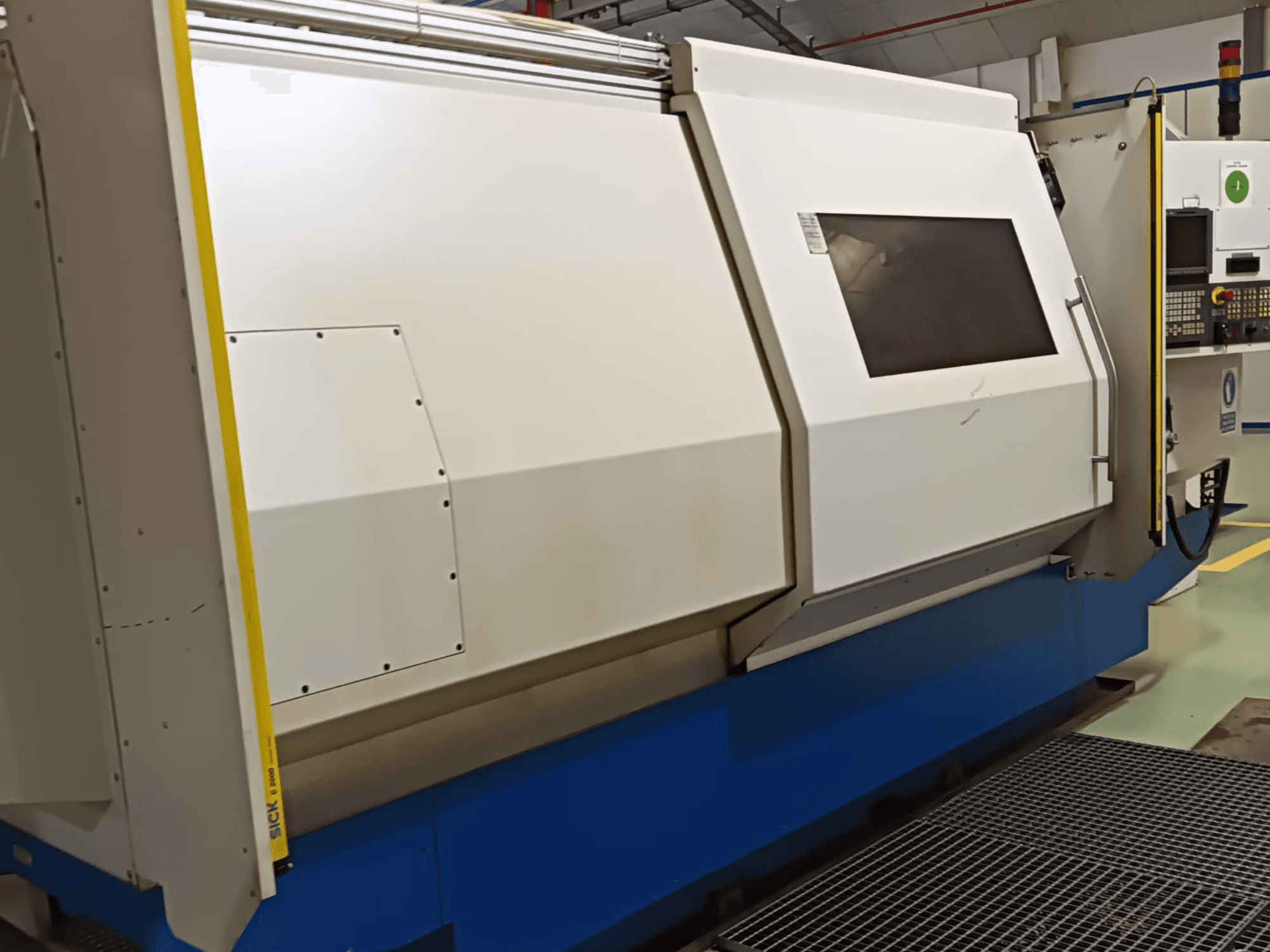 Industrielle Drehmaschine, Seitenansicht, mit einem großen weiß-blauen Gehäuse, digitalem Bedienfeld und Sicherheitsfunktionen.