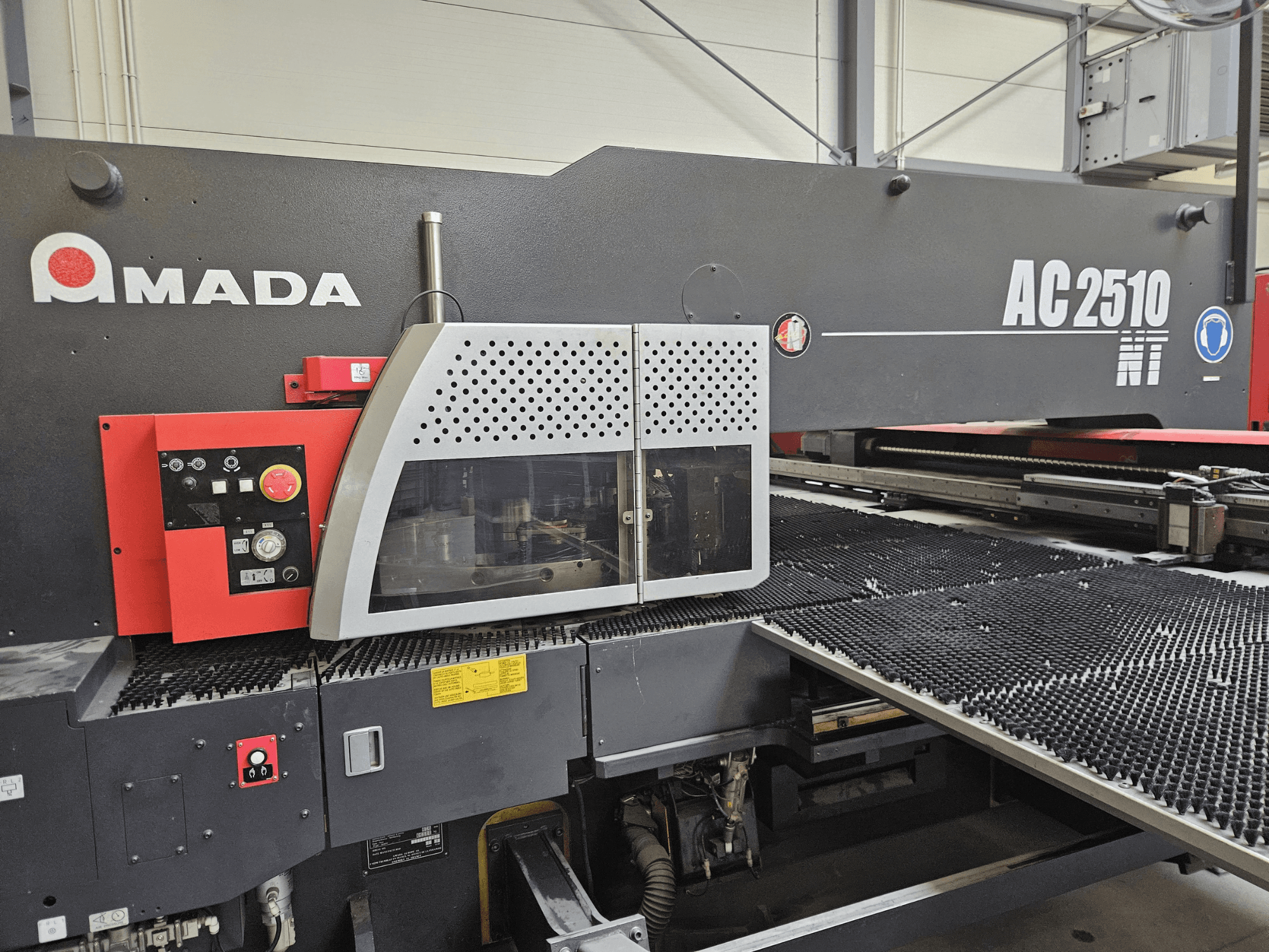 Amada AC2510 NT Laserschneidmaschine, Vorderansicht, mit Bedienfeld mit Knöpfen, Tasten und einer Sicherheitsabdeckung.