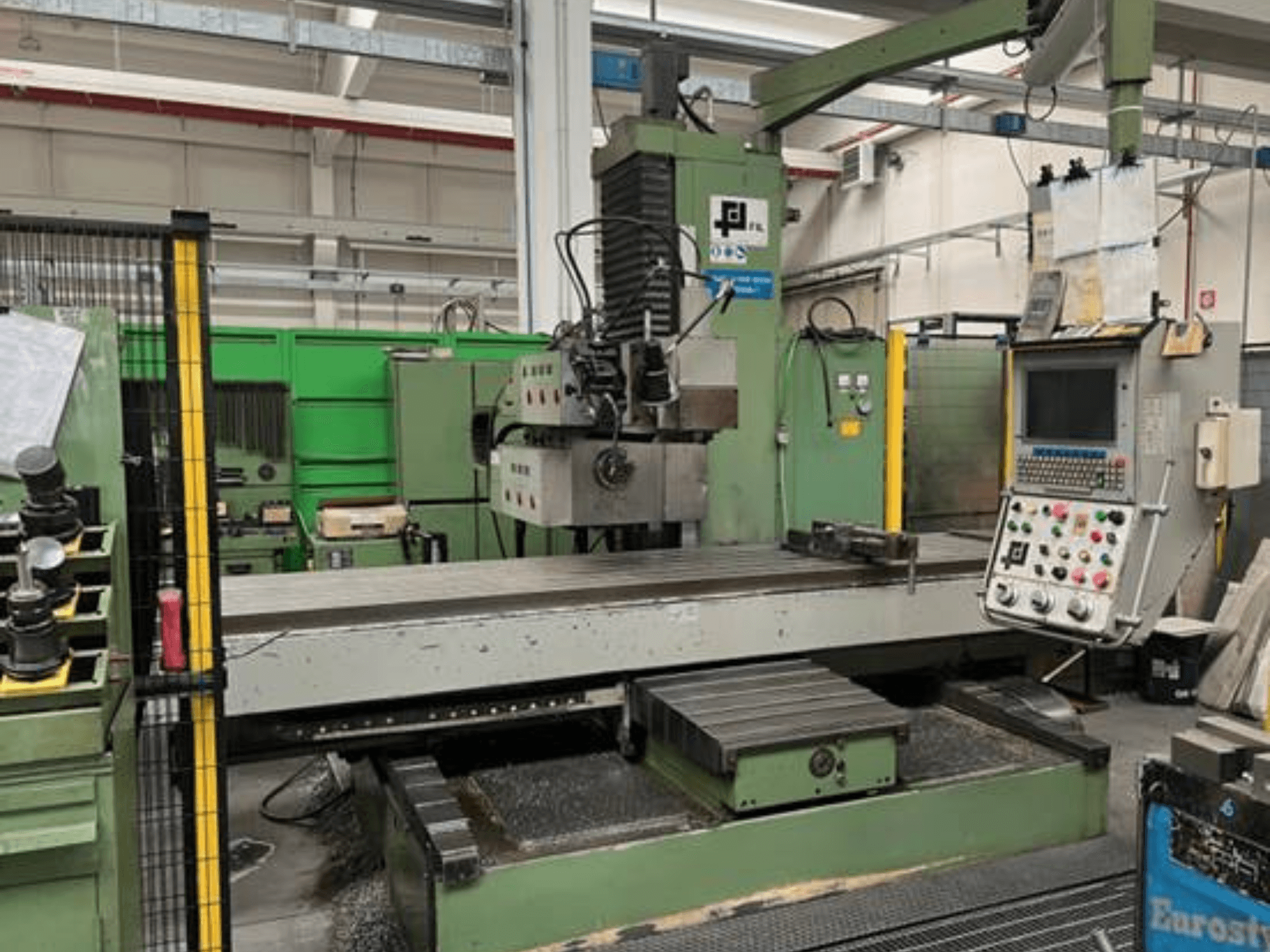 Industriefräsmaschine von JFL, Vorderansicht mit Bedienfeld, großem flachen Tisch und Metallspänen auf dem Boden.