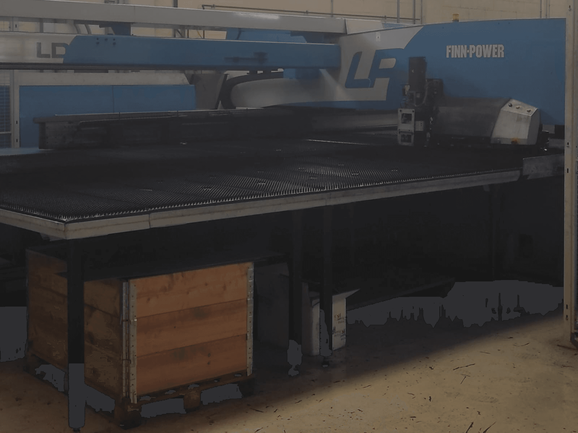 Finn-Power LP-Schneidemaschine in einer Fabrik, Vorderansicht mit einem strukturierten Metalltisch und einer Holzkiste darunter.
