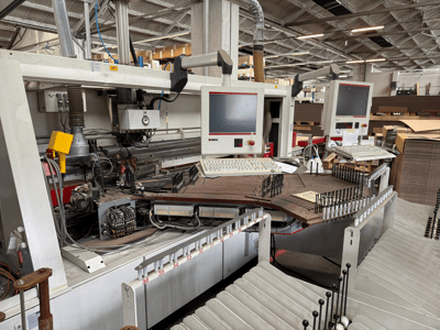 IMA-Präzisionsholzbearbeitungsmaschine mit zwei Monitoren und Bedienfeldern, Vorderansicht mit Förderband und Werkzeugbereich.