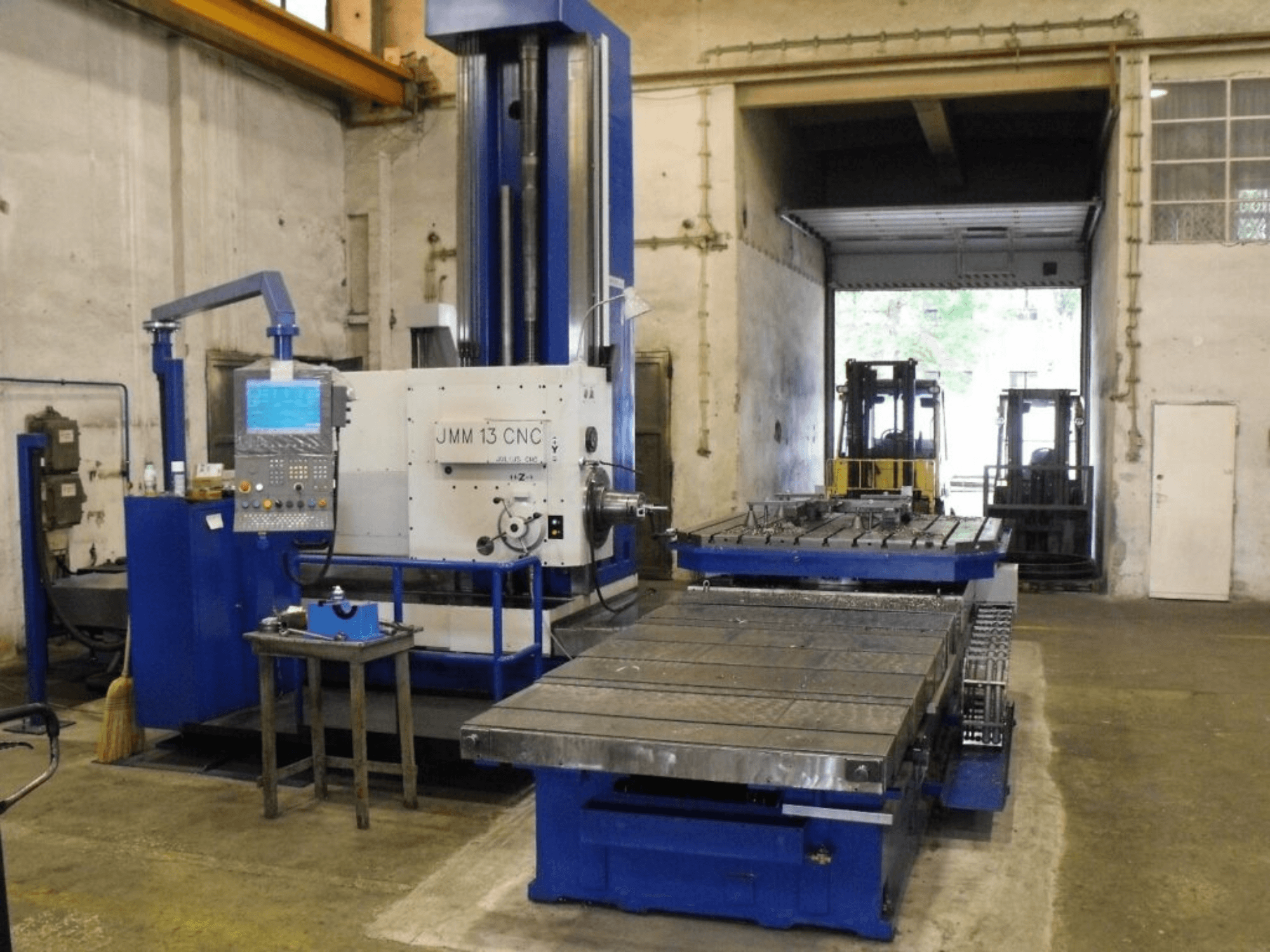 CNC-Fräsmaschine JMM 13 in einer Werkstatt, Vorderansicht, mit Bedienfeld, großem Arbeitstisch und Industriekulisse.