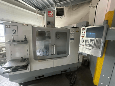 Haas VF-2 CNC-Maschine, Vorderansicht, mit Bedienelementen, Werkzeughalter und durchsichtigen Türen mit sichtbaren Werkzeugen im Inneren des Gehäuses.