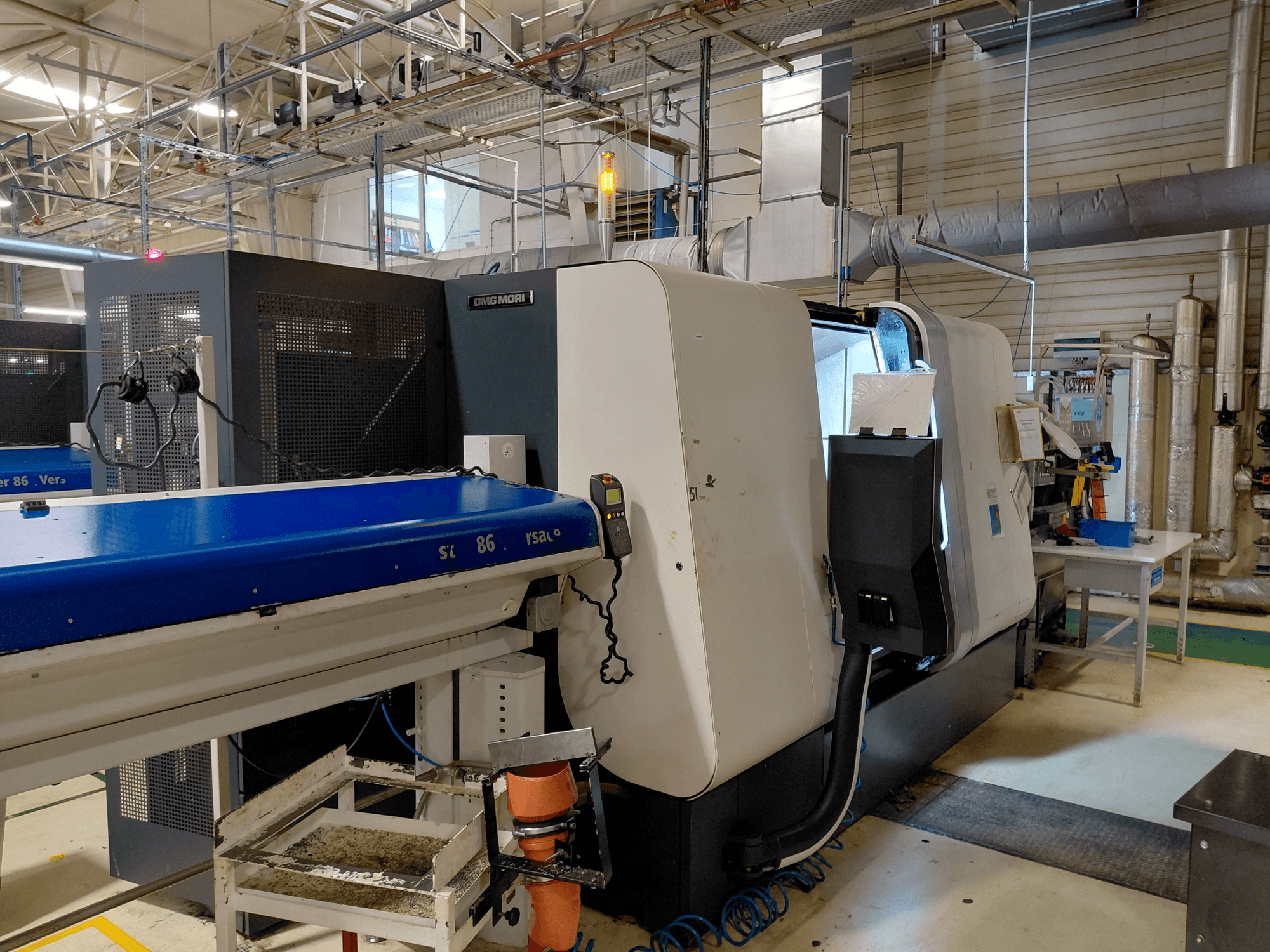 DMG MORI Sprint 65 Linear-Mehrspindeldrehmaschine, Seitenansicht mit Bedienpult und Förderband in einer Werkstattumgebung.