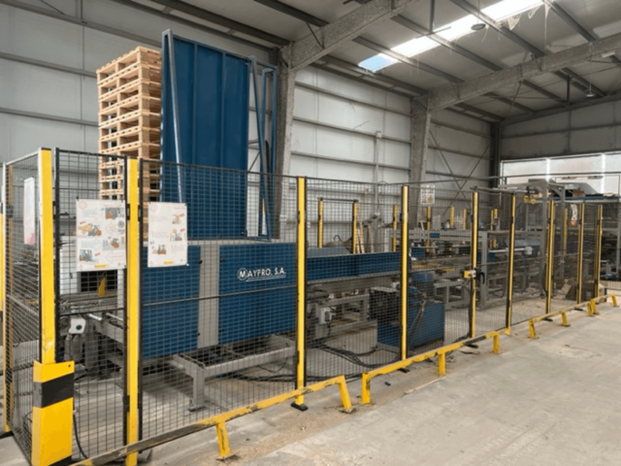 Industrial pallet packaging machine by Maypro S.A. in a warehouse, featuring safety mesh and operational controls, side view.