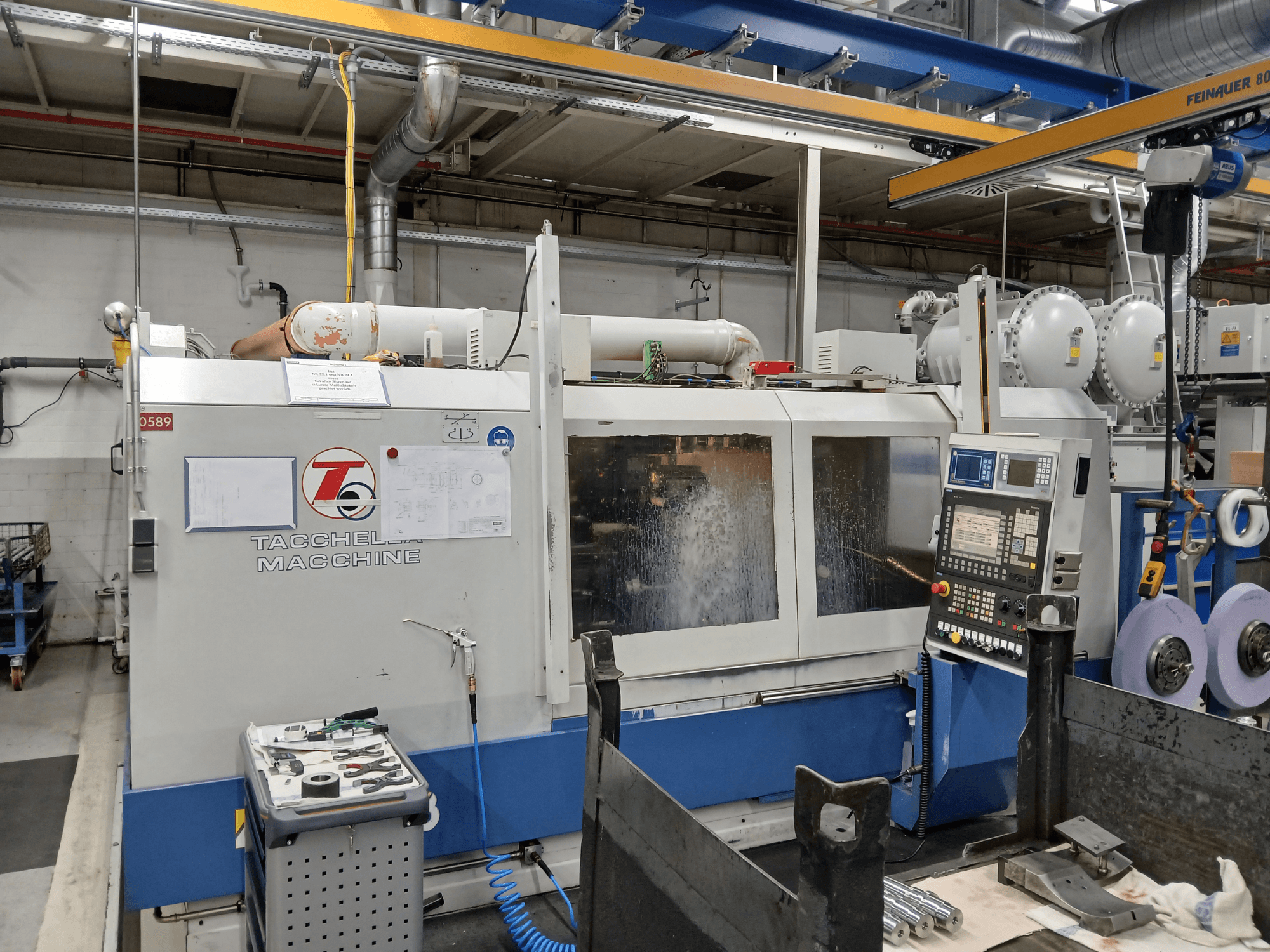 Tacchella-Bearbeitungszentrum aus der Vorderansicht, mit Bedienfeld und Werkzeugen sichtbar. Wasser-Kühlmittel spritzt während des Betriebs.