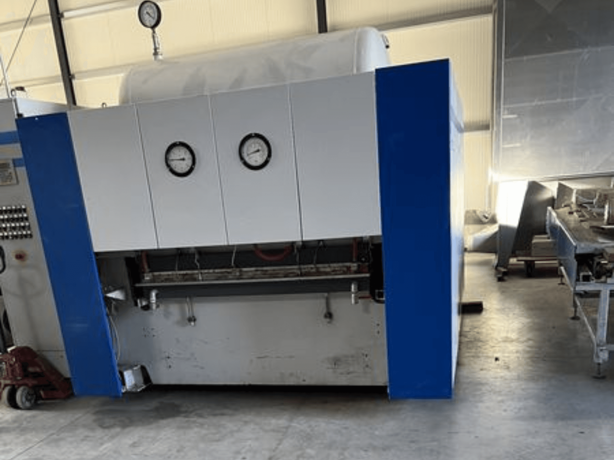 Blau-weiße Industriemaschine mit zwei Manometern, Vorderansicht, mit einem Bedienfeld und angrenzenden Geräten.