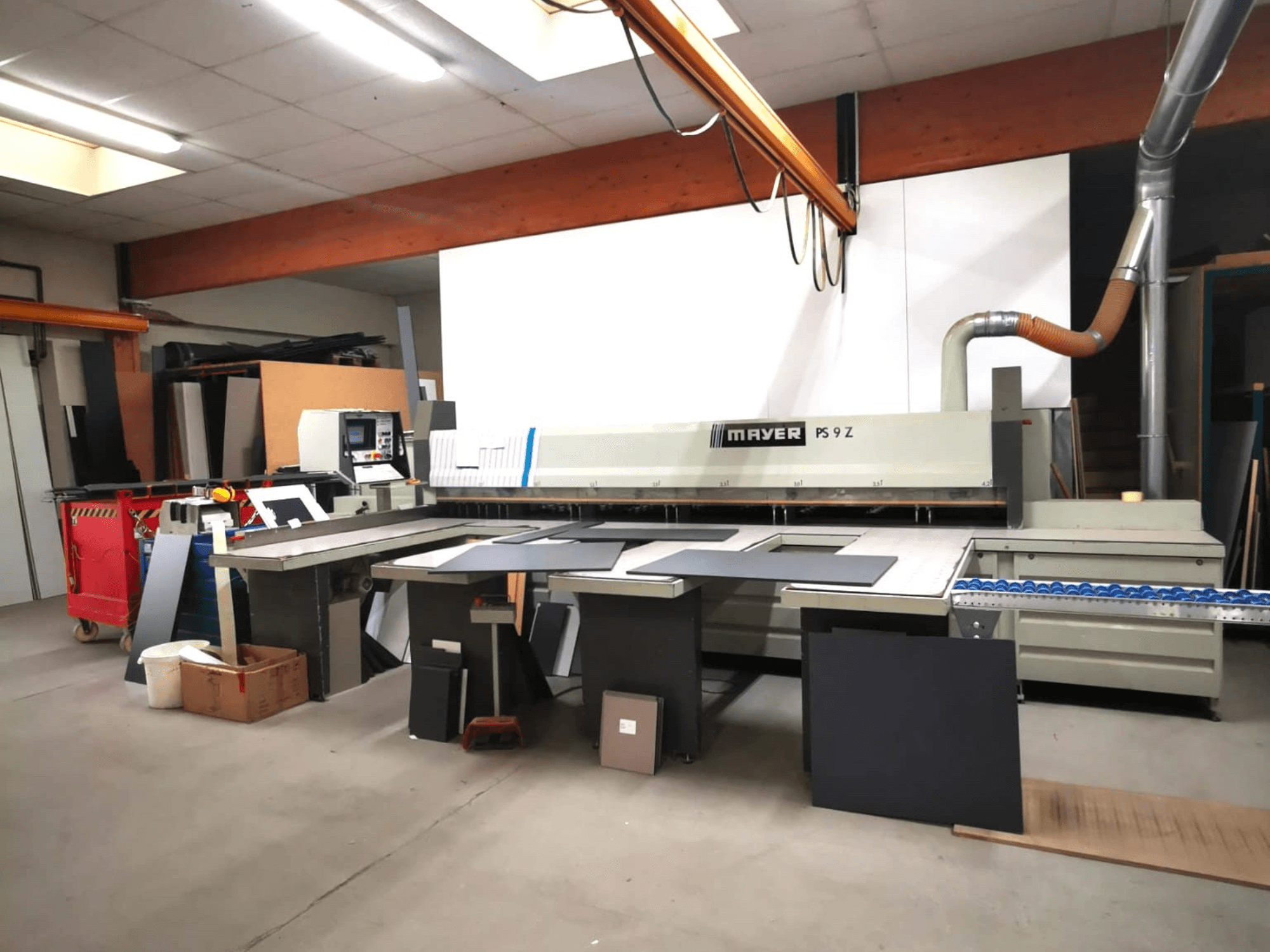 MAYER PS9 Z-Schneidemaschine in einer Werkstatt, Vorderansicht, mit verschiedenen Materialien und einem Fördersystem sichtbar.
