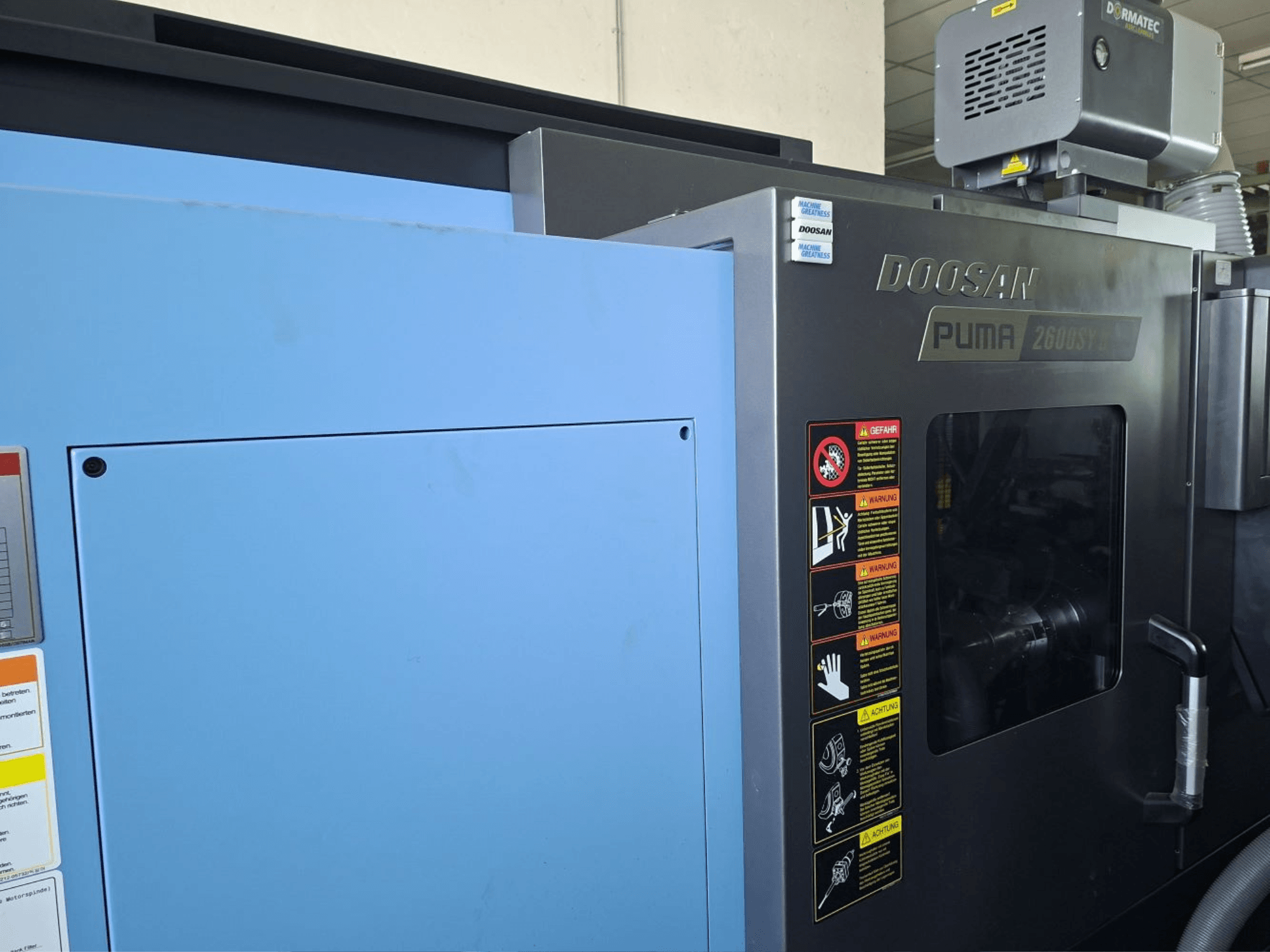 DOOSAN PUMA 2600 SY II Horizontaldrehmaschine, Vorderansicht, mit Sicherheitsetiketten und blauer Verkleidung.
