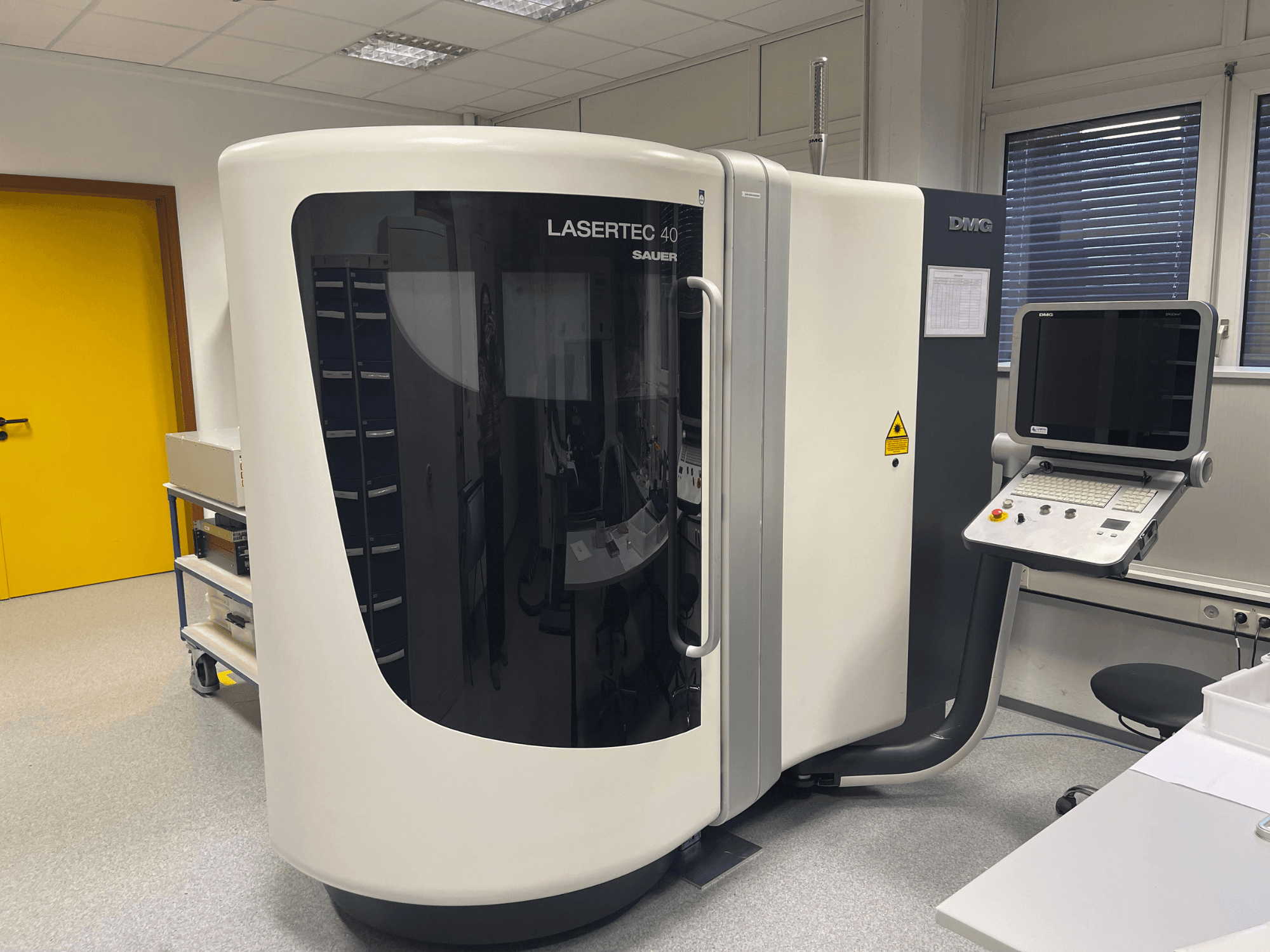 Weiße LASERTEC 40 Fräsmaschine von DMG MORI, Frontansicht, mit Bedienfeld und ergonomischem Design in einem gut ausgeleuchteten Raum.