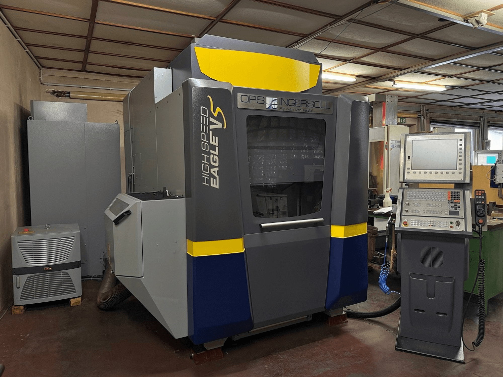 High Speed Eagle V machine by OPS Ingersoll, side view, with control panel and adjacent equipment in industrial setting.