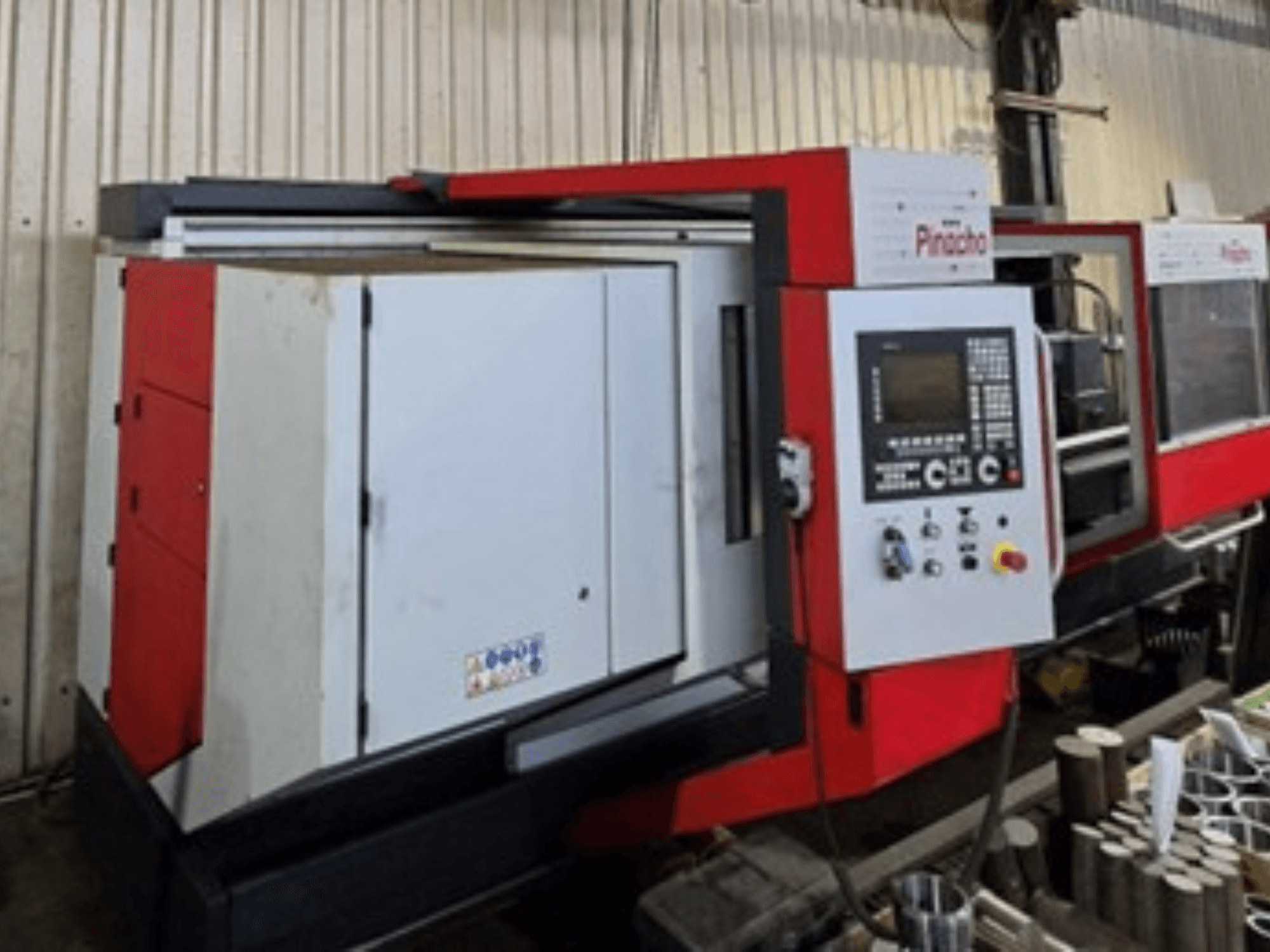 Pinacho CNC-Maschine in Rot und Weiß, Seitenansicht, mit Bedienfeld und Materialien auf dem Boden, zeigt die Betriebseinrichtung.