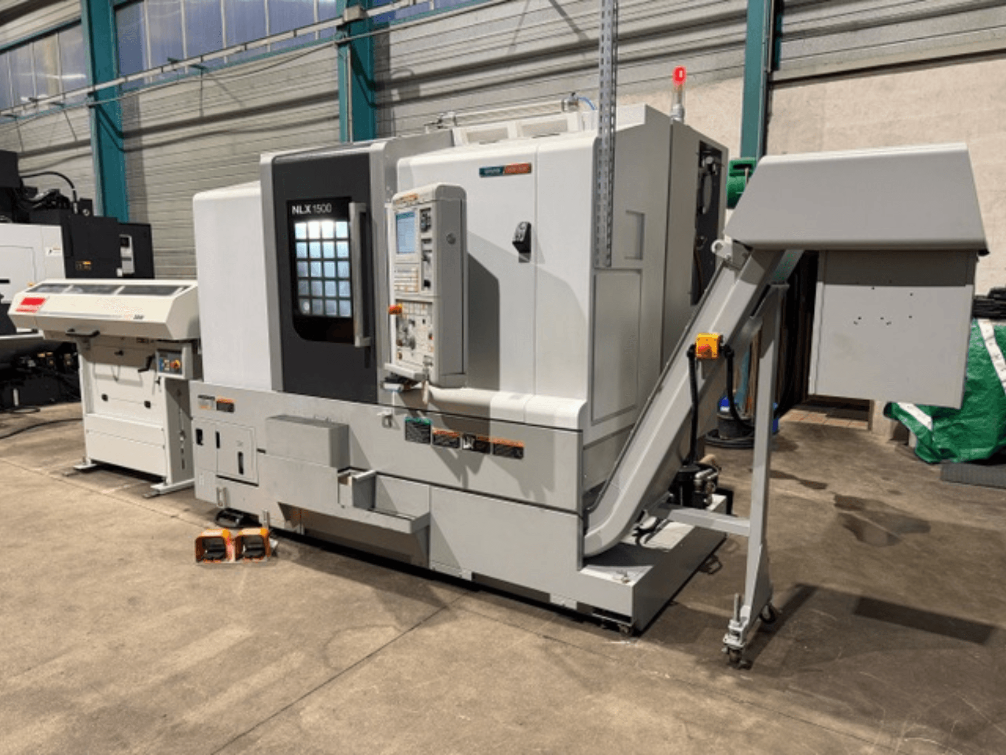 CNC-Maschine NLK 1500, Vorderansicht, mit Bedienfeld und Zubehörtrichter an der Seite, auf Betonboden liegend.