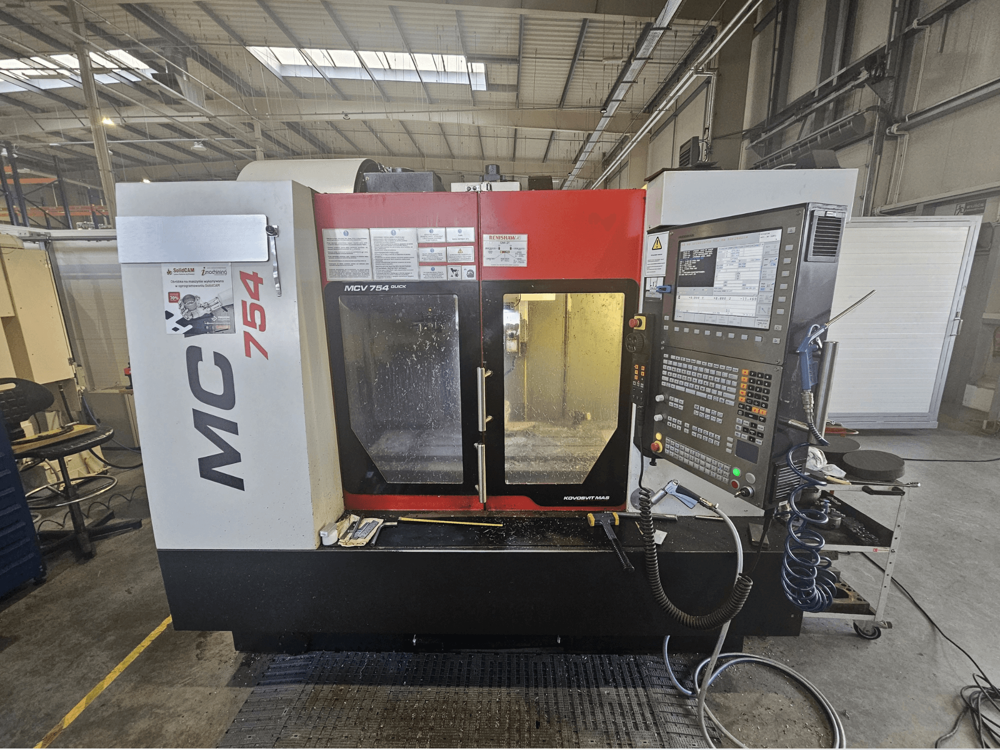 Die CNC-Fräsmaschine MC 754 in der Vorderansicht verfügt über ein Bedienfeld mit Tasten, Bildschirmen und einem Arbeitsbereich mit Kühlmittel.