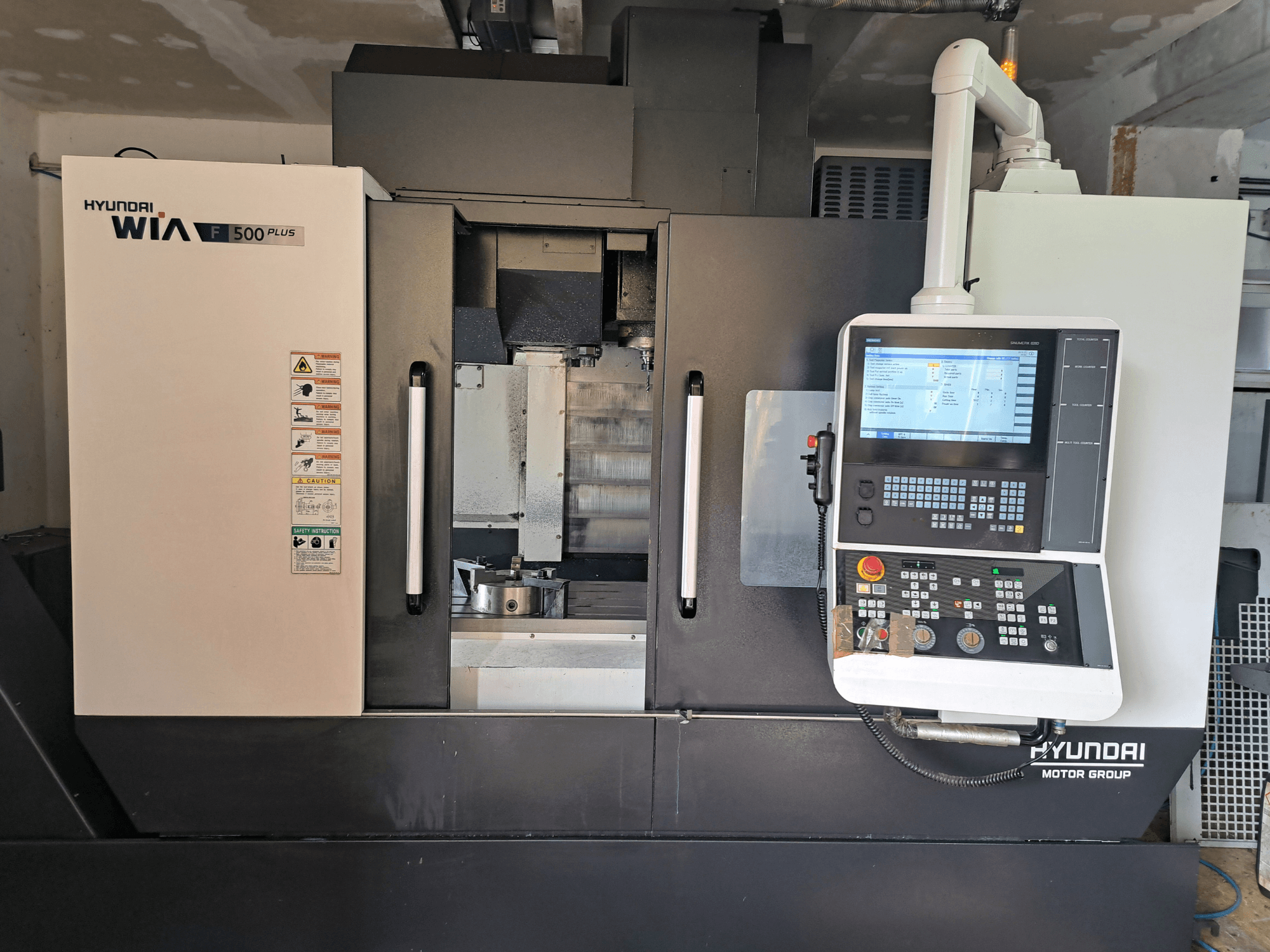 Hyundai WIA F500 Plus CNC-Maschine in der Vorderansicht, mit digitalem Bedienfeld und Sicherheitsschildern.
