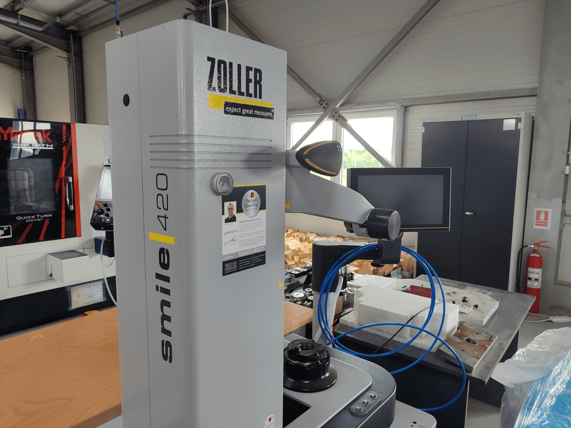 ZOLLER smile 420 measuring device with monitor, side view in a workshop, featuring blue hoses and machinery in the background.