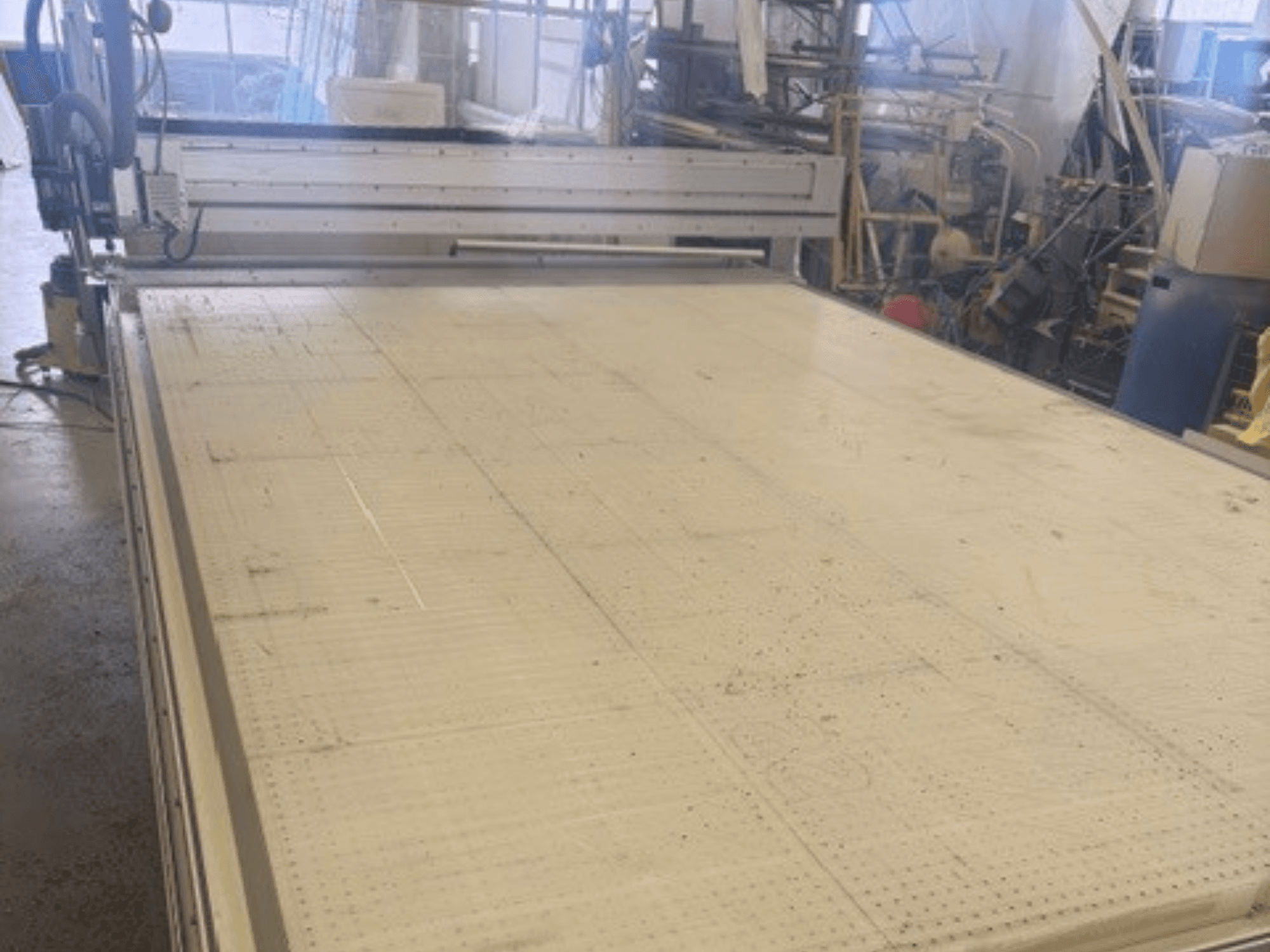 Large cutting machine with a flat surface, showing frame and guide rail; viewed from an angle in a workshop setting.