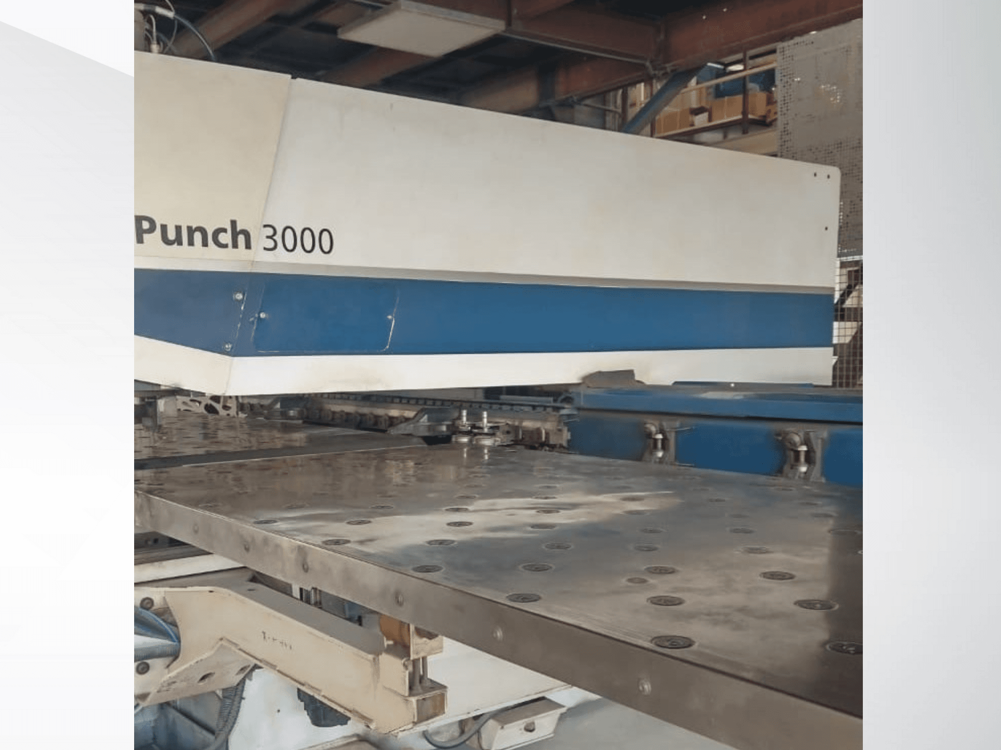 Punch-3000-Maschine in einer Werkstatt, Vorderansicht, zeigt eine große, flache Metallfläche mit mehreren Stanzlöchern.