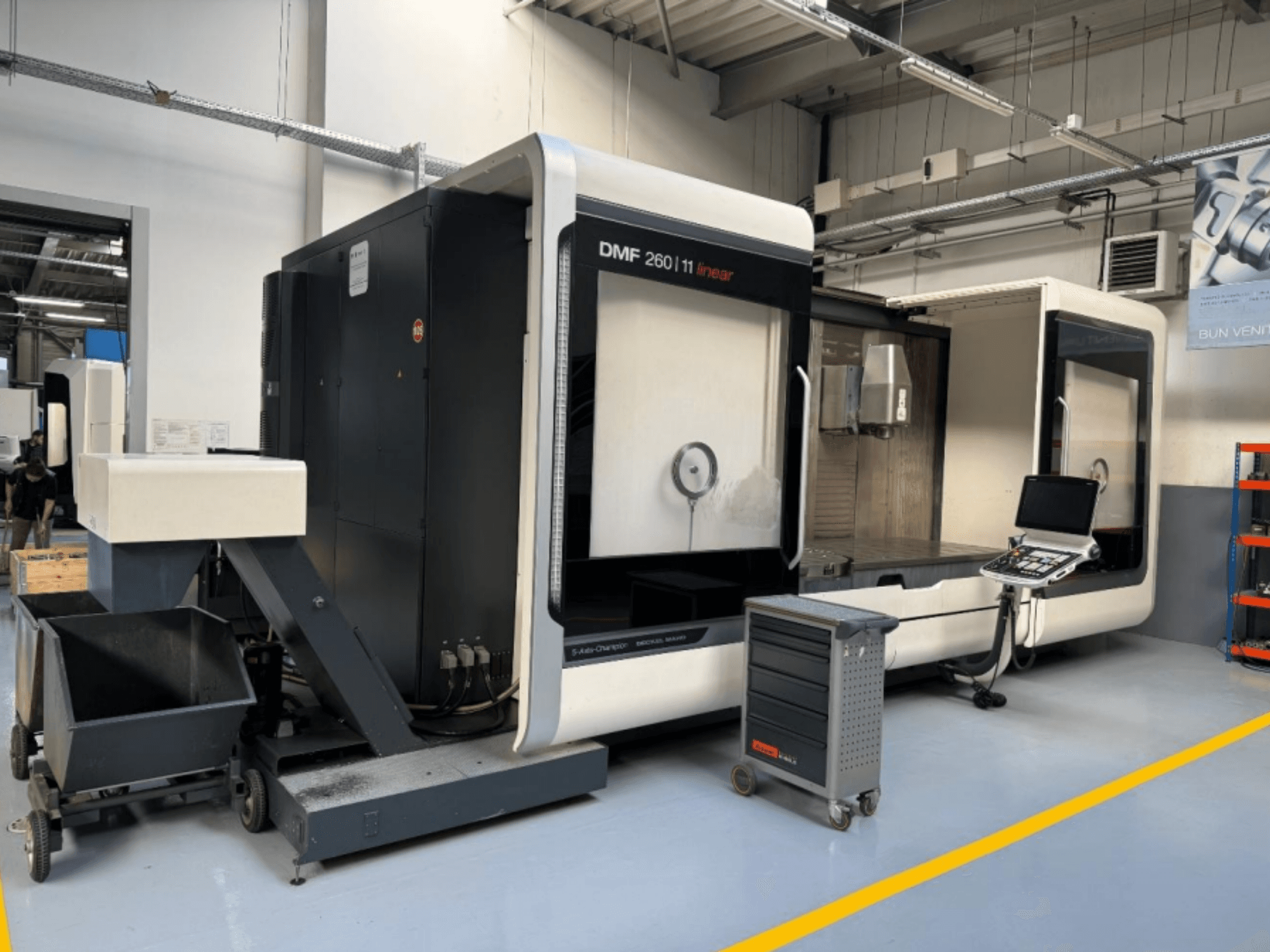 DMG MORI DMF 260 Linear-Fräsmaschine in der Frontansicht, mit einem Werkzeugbedienfeld und einem mobilen Werkzeugwagen in der Nähe.